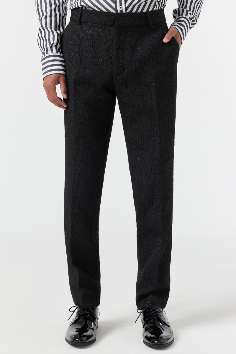 A person wearing the Clyde Slim Trouser - Metallic Groove, paired with a black and white striped shirt and shiny black dress shoes, stands against a plain white background. The image shows them cropped from the shoulders down.