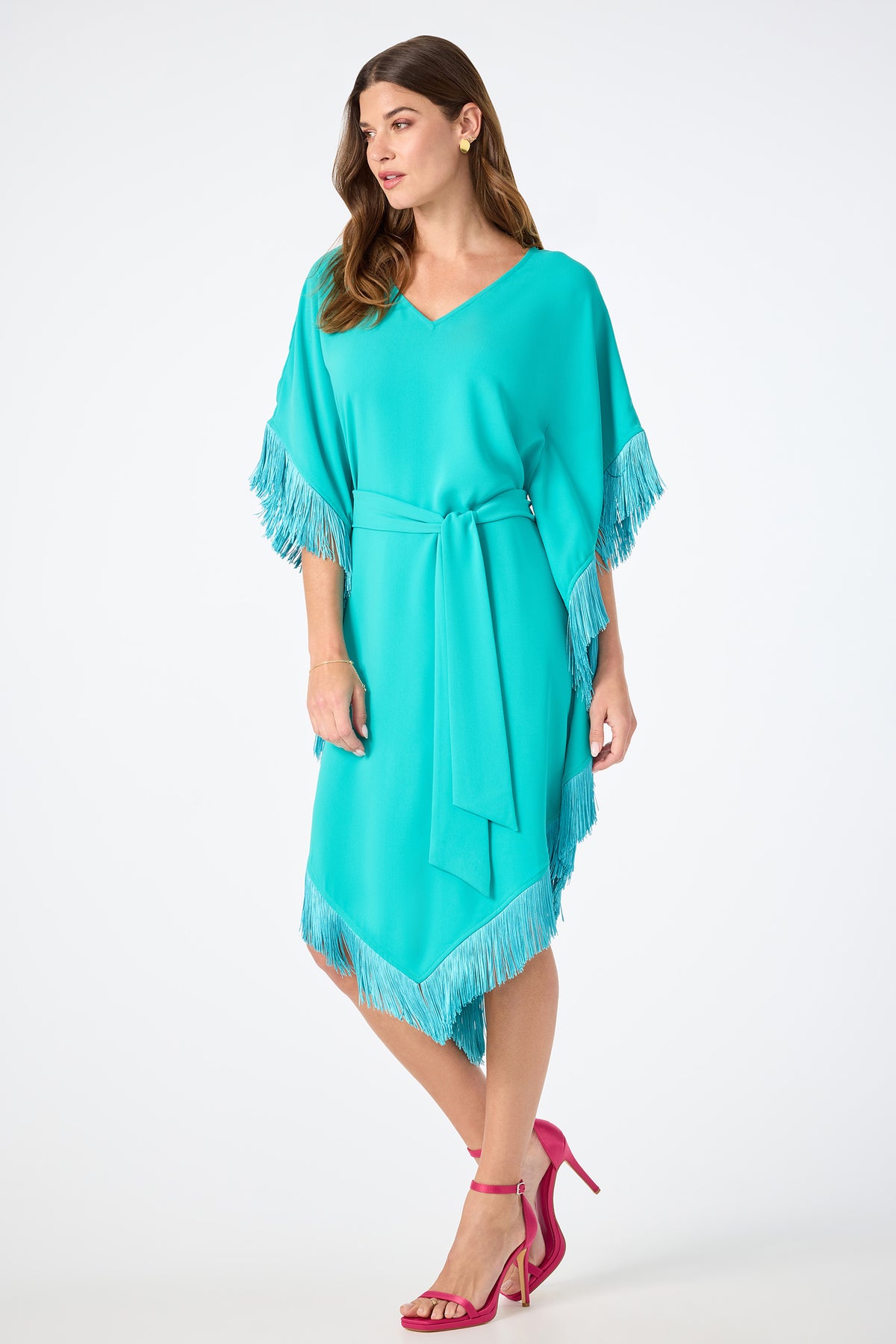 A woman wearing the Toulouse Short-Sleeve Fringe Dress, featuring fringe details on the sleeves and hem with a matching waist tie, pairs it with pink high-heeled sandals and stands against a plain white background.