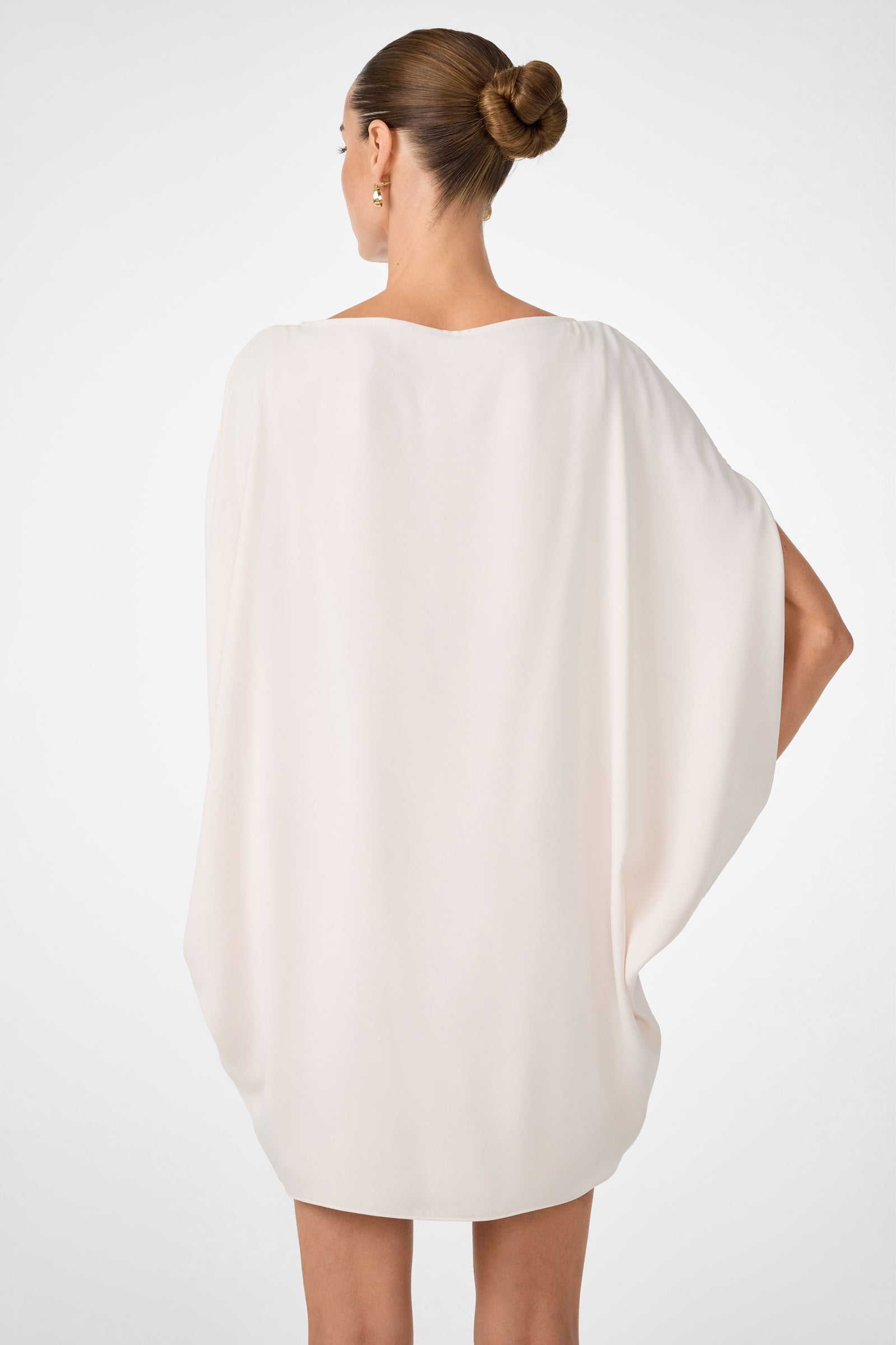 A woman with her hair in a bun models the Razu Short Split Sleeve Mini Dress in white, shown from the back with one hand on her hip against a plain, light background.