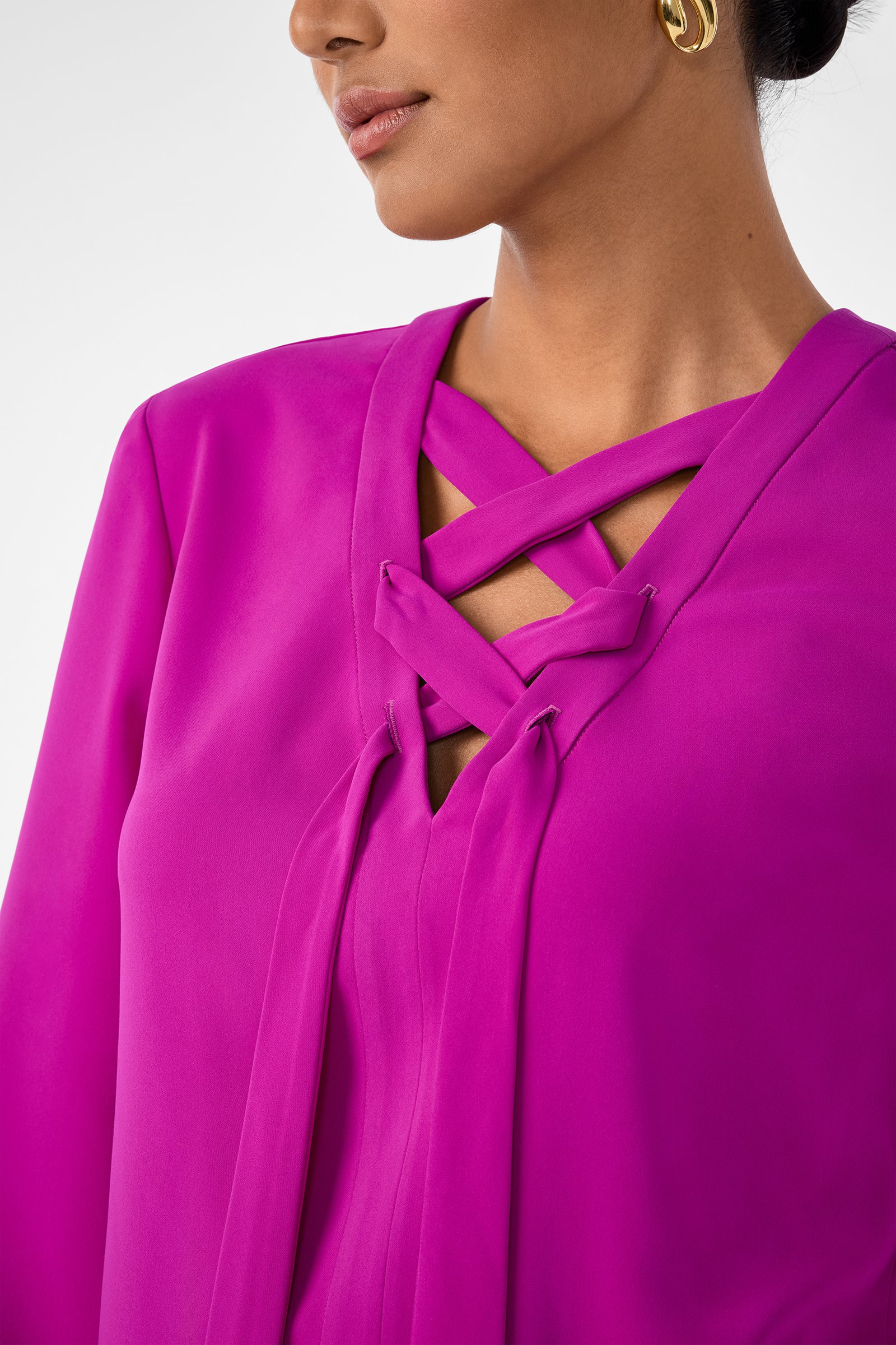 A woman wears the Picabella Top in bright magenta with a crisscross neckline and gold hoop earrings, showing only her lower face and upper torso.