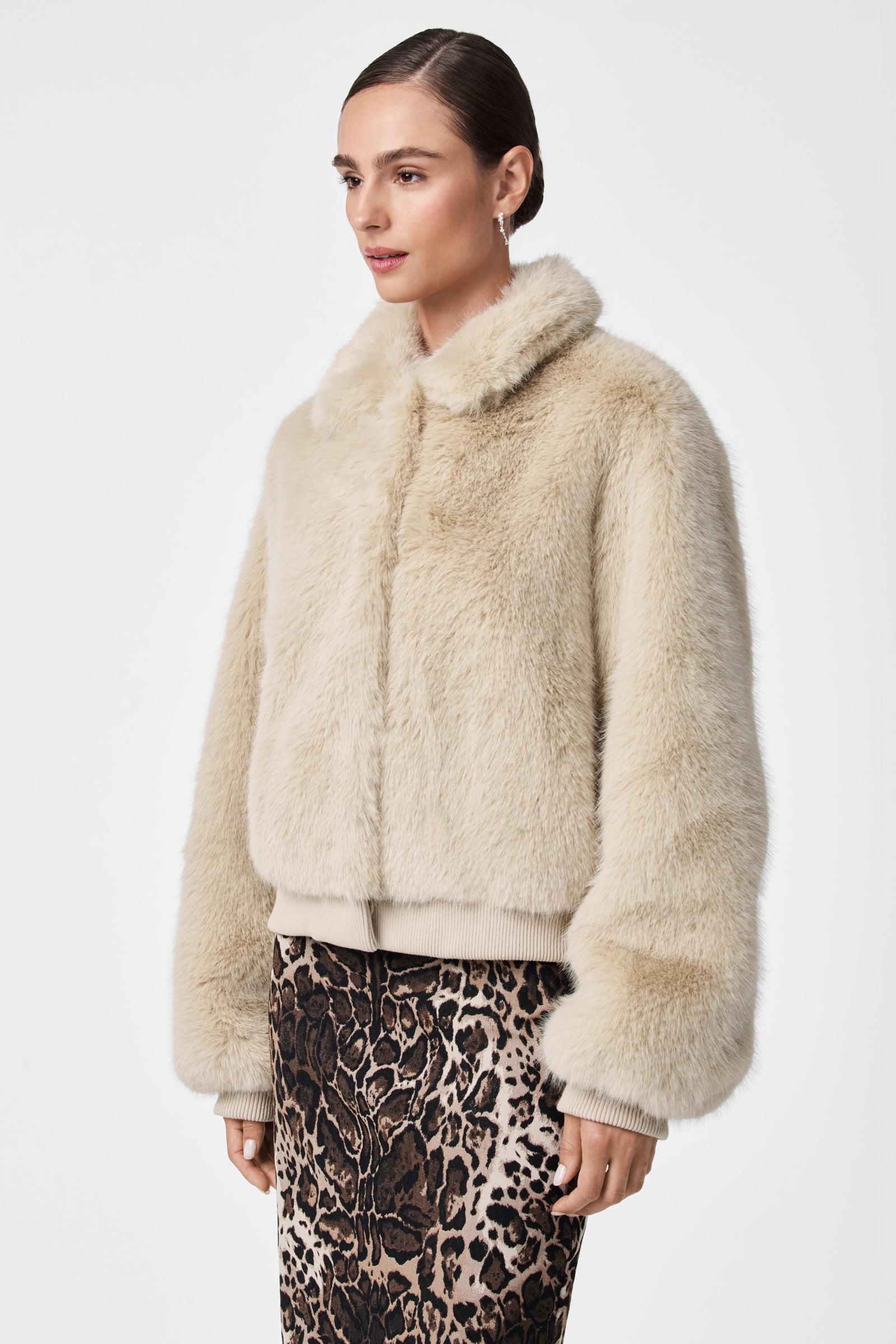 A woman with slicked-back hair wears the Morris Short Faux Fur Coat in light beige and a high-waisted leopard print skirt, standing against a plain white background.