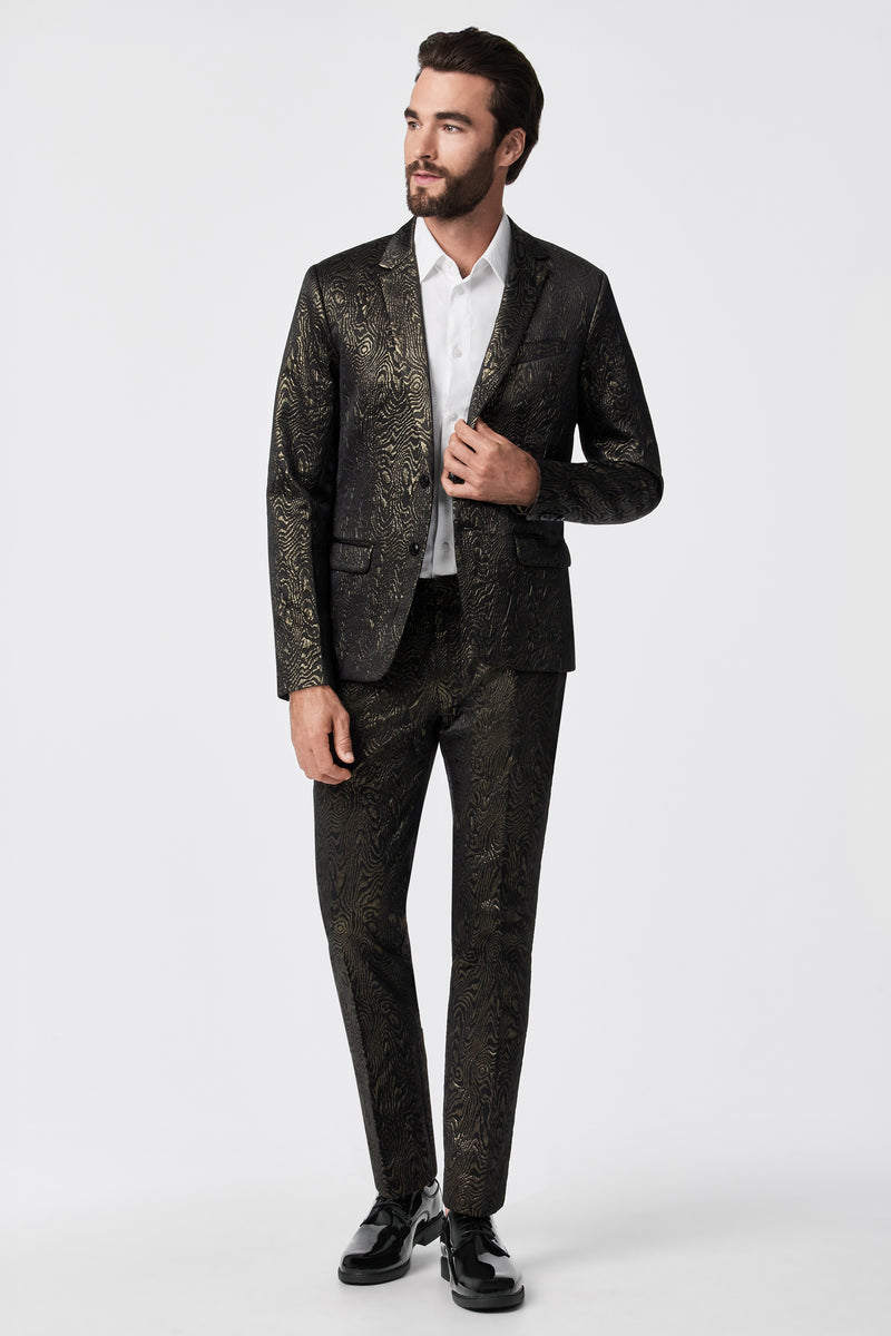 A man with dark hair and a beard wears the Clyde Slim Trouser - Fette Swirl with a white dress shirt and black shoes, standing against a plain white background.