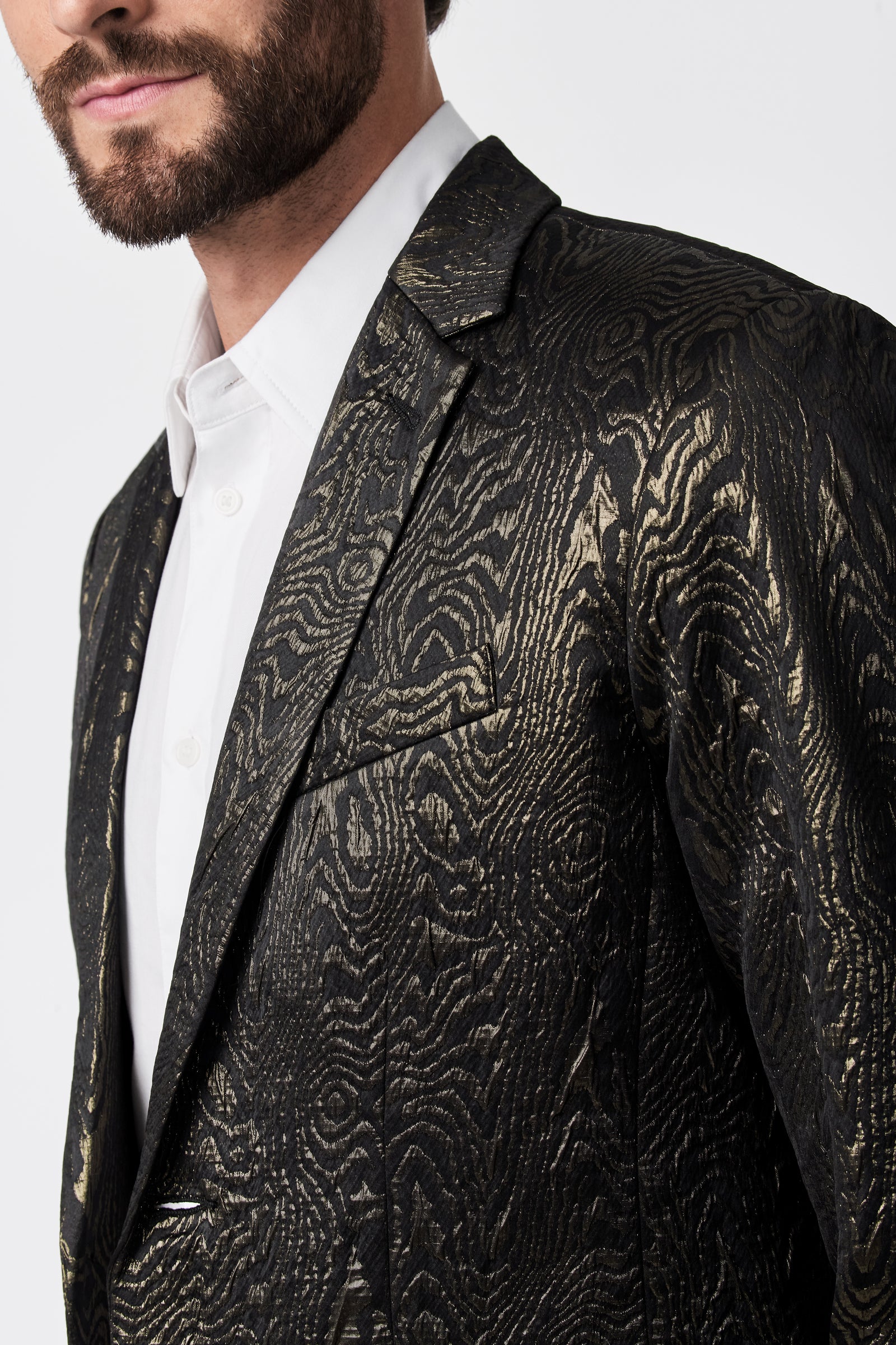 Close-up of a man wearing the Thurston Blazer - Fette Swirl, featuring a shiny gold textured pattern over a white shirt. Only his lower face and upper body are shown against a plain background.