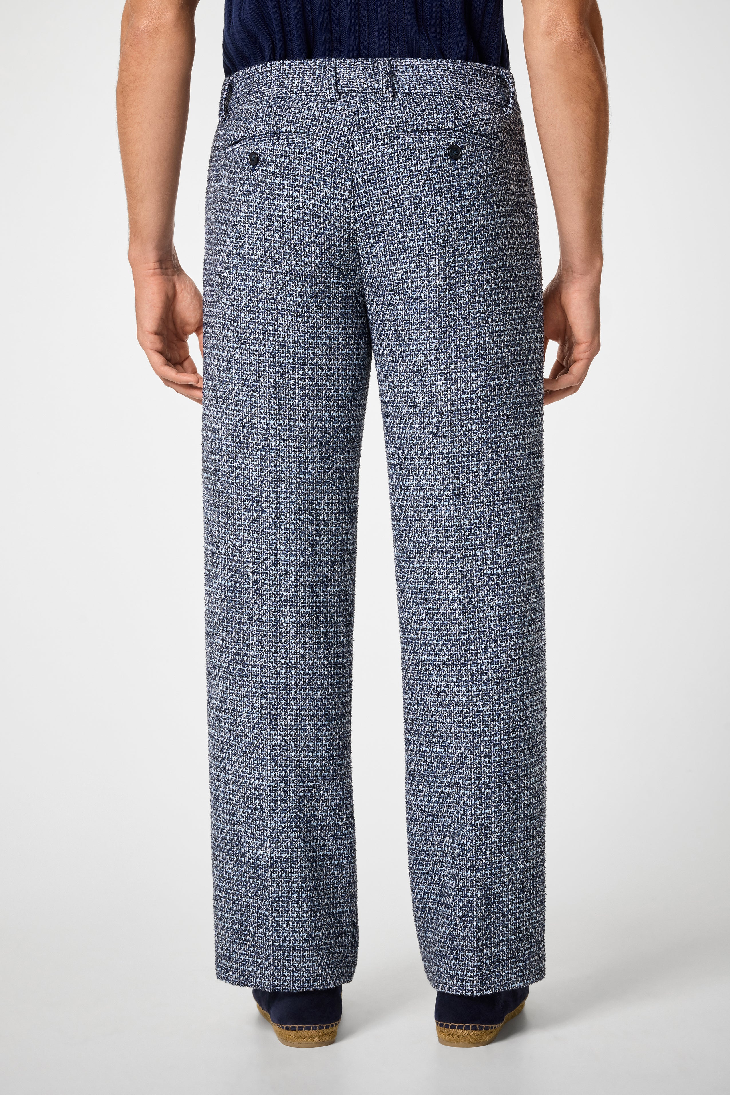 A person is seen from behind, wearing the Buckingham Trouser—textured blue and white wide-leg pants with two back pockets and dark buttons—standing against a plain white background.