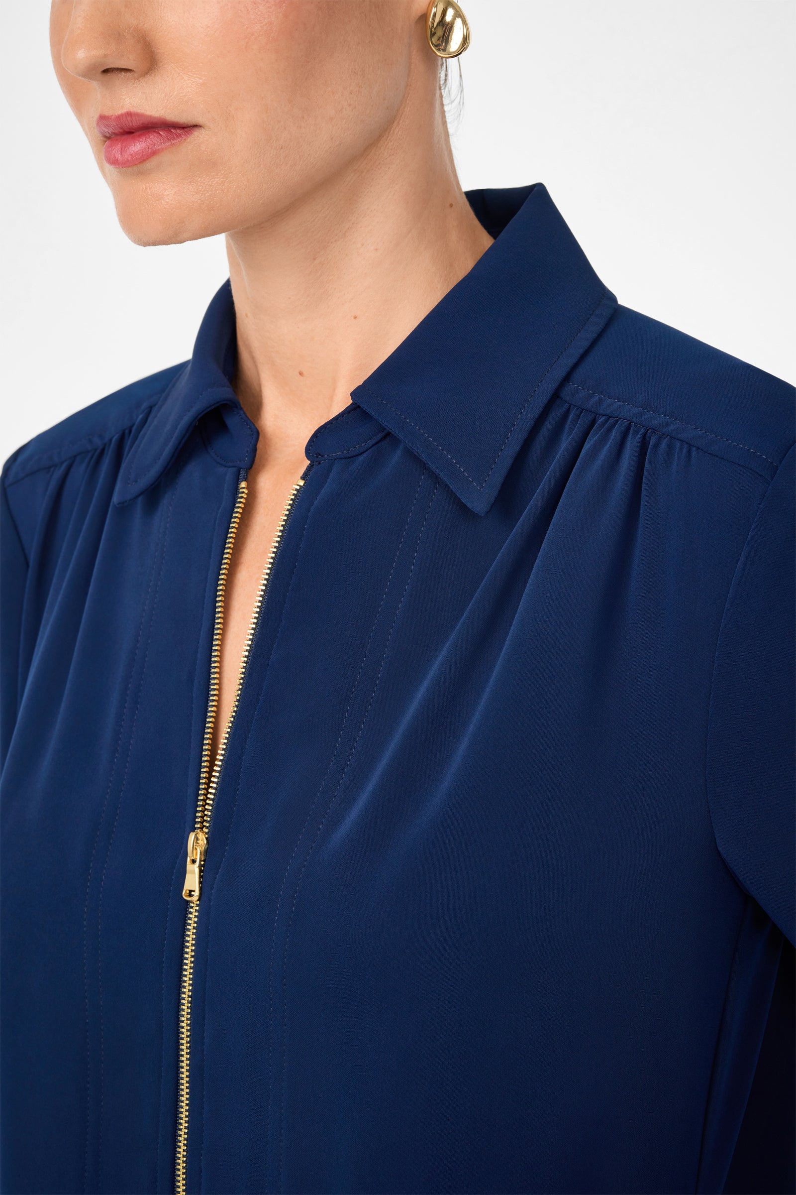 A woman in the Darya Long-Sleeve Dress with a gold zipper, gold hoop earrings, and light pink lipstick. The image shows her from the shoulders up, face turned slightly to the side.