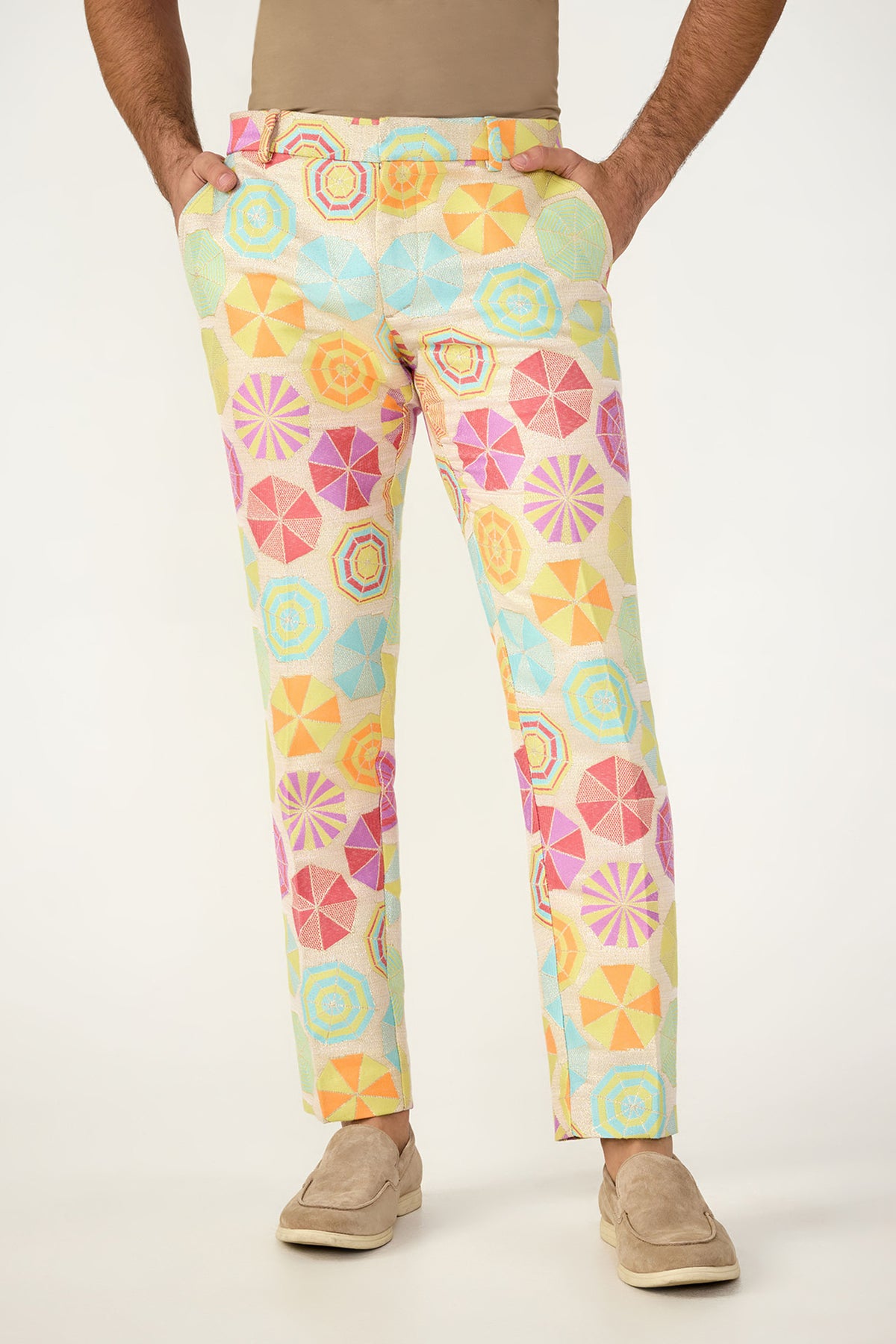 A person wears the Clyde Slim Trouser in Parapluie Jacquard—pastel pants with a bold, geometric umbrella pattern—paired with a beige shirt and tan slip-ons. The upper body is cropped out of the image.