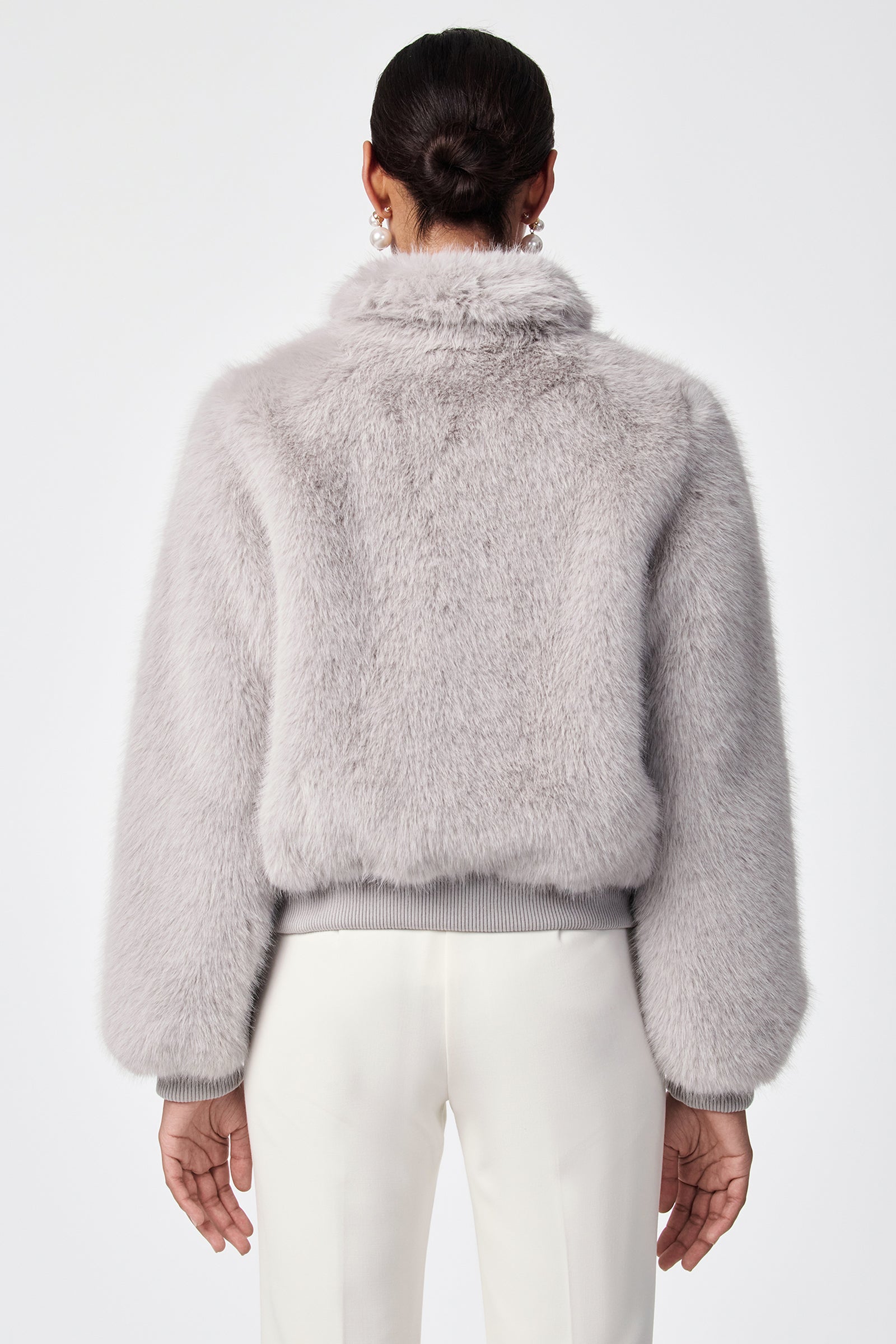 A person with dark hair in a low bun is shown from the back, wearing the Morris Short Faux Fur Coat in light gray and white pants against a plain white background.