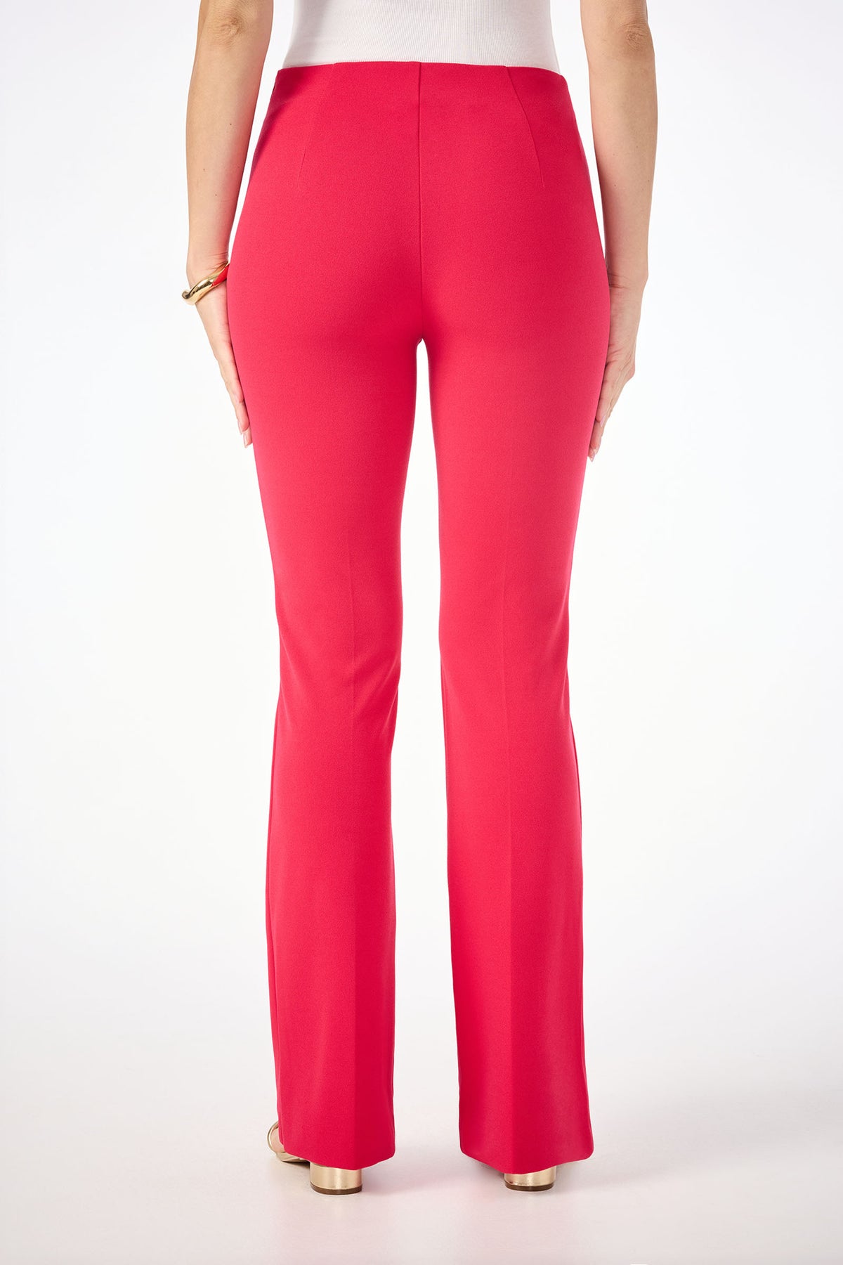 A woman faces away from the camera wearing Jacoba Slim-Fit Bootcut Pants in bright pink, paired with a white top and a gold bracelet. The background is plain white.