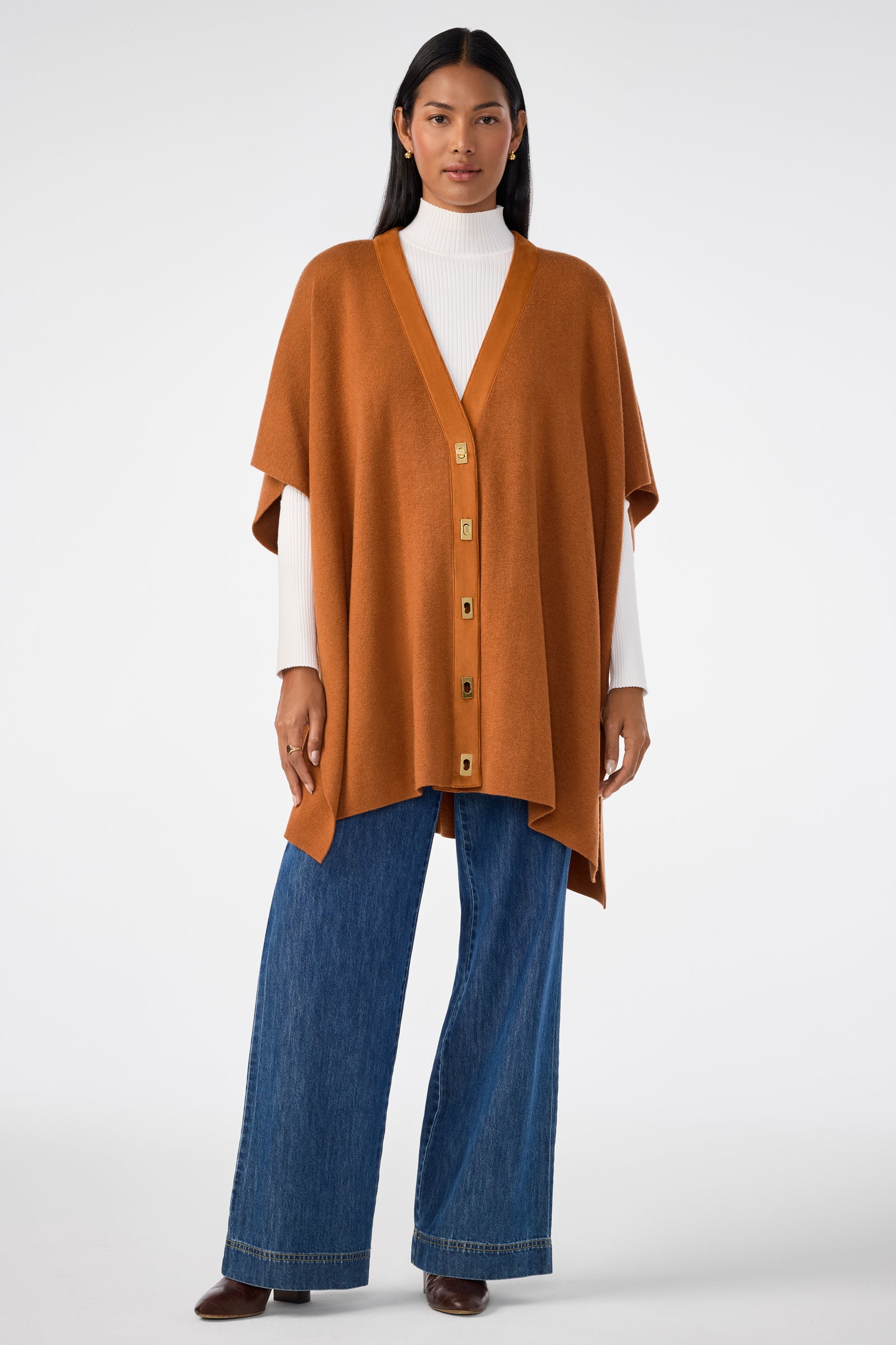 A woman models the Sapphire Poncho over a white turtleneck, wide-leg blue jeans, and brown shoes, standing against a plain white background.