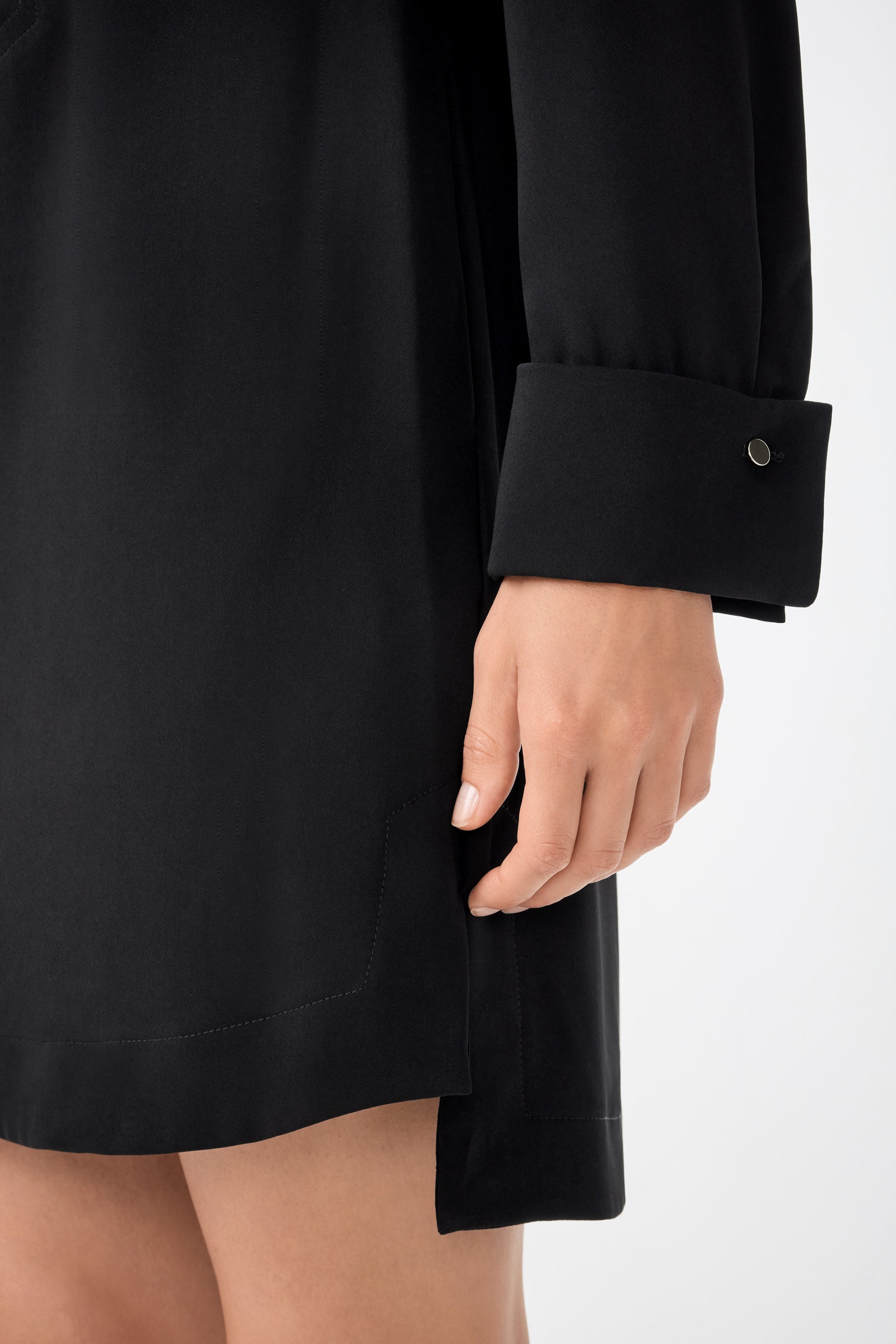 A close-up of a person wearing the Darya Long-Sleeve Dress in black, highlighting the cuff with a button and their hand by their side. The photo emphasizes the dresss fabric and detailed sleeve design.