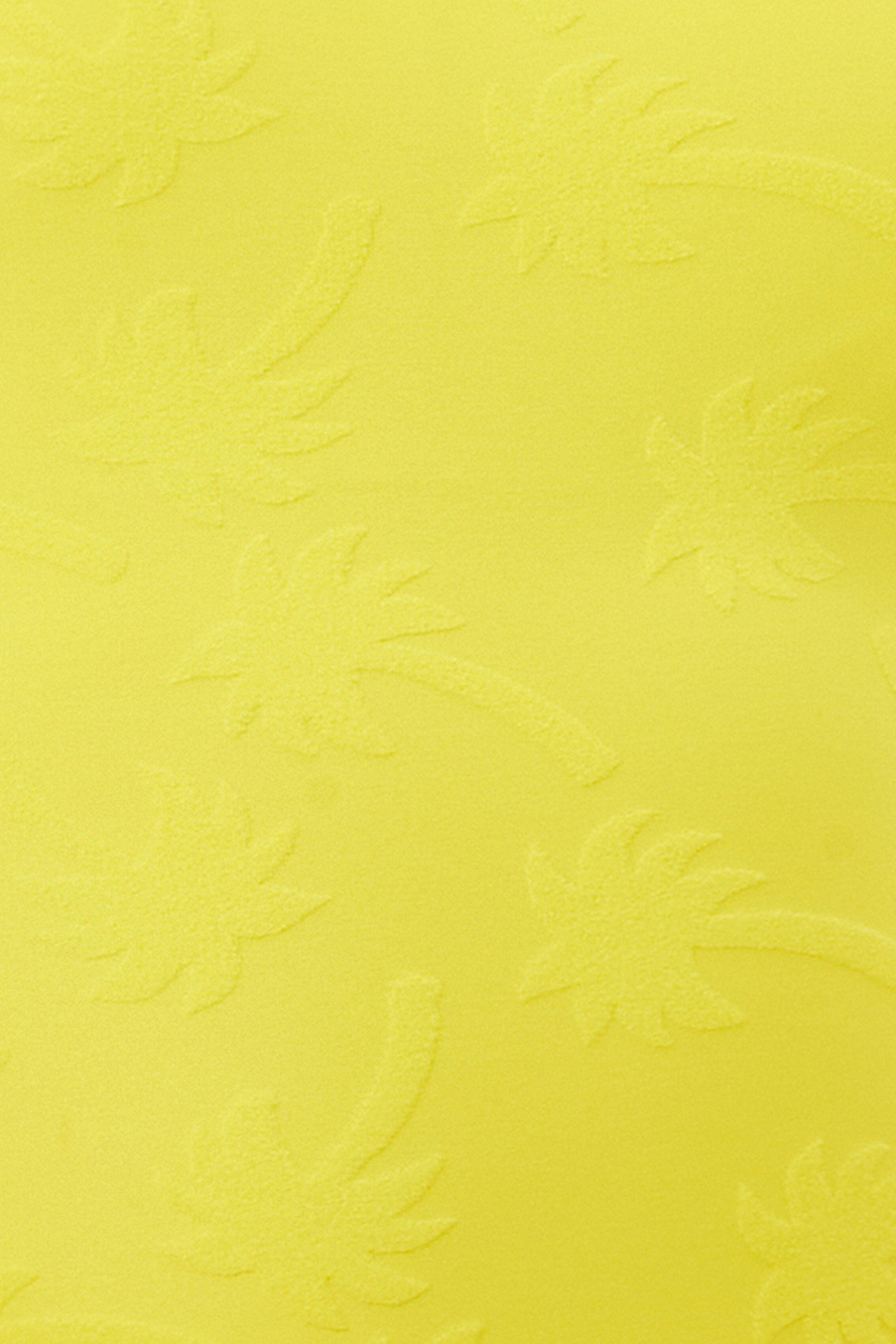 The Women's Sway Ruffle Plunge One Piece Swimsuit showcases a bright yellow surface with a subtle embossed palm tree pattern, adding textured, tropical flair.