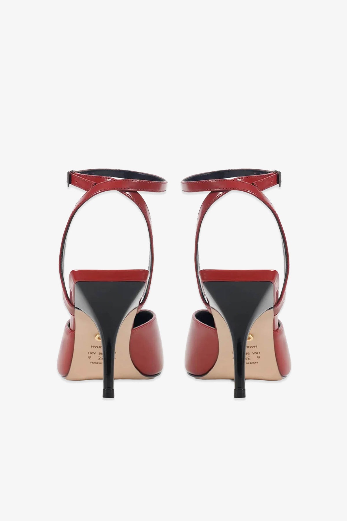 A pair of Paula Torres Cannes Pump high-heeled shoes with ankle straps, displayed from the back against a white background. With their elegant pointed toes, black heels and soles, and glossy red finish, these luxury pumps exude sophisticated appeal.