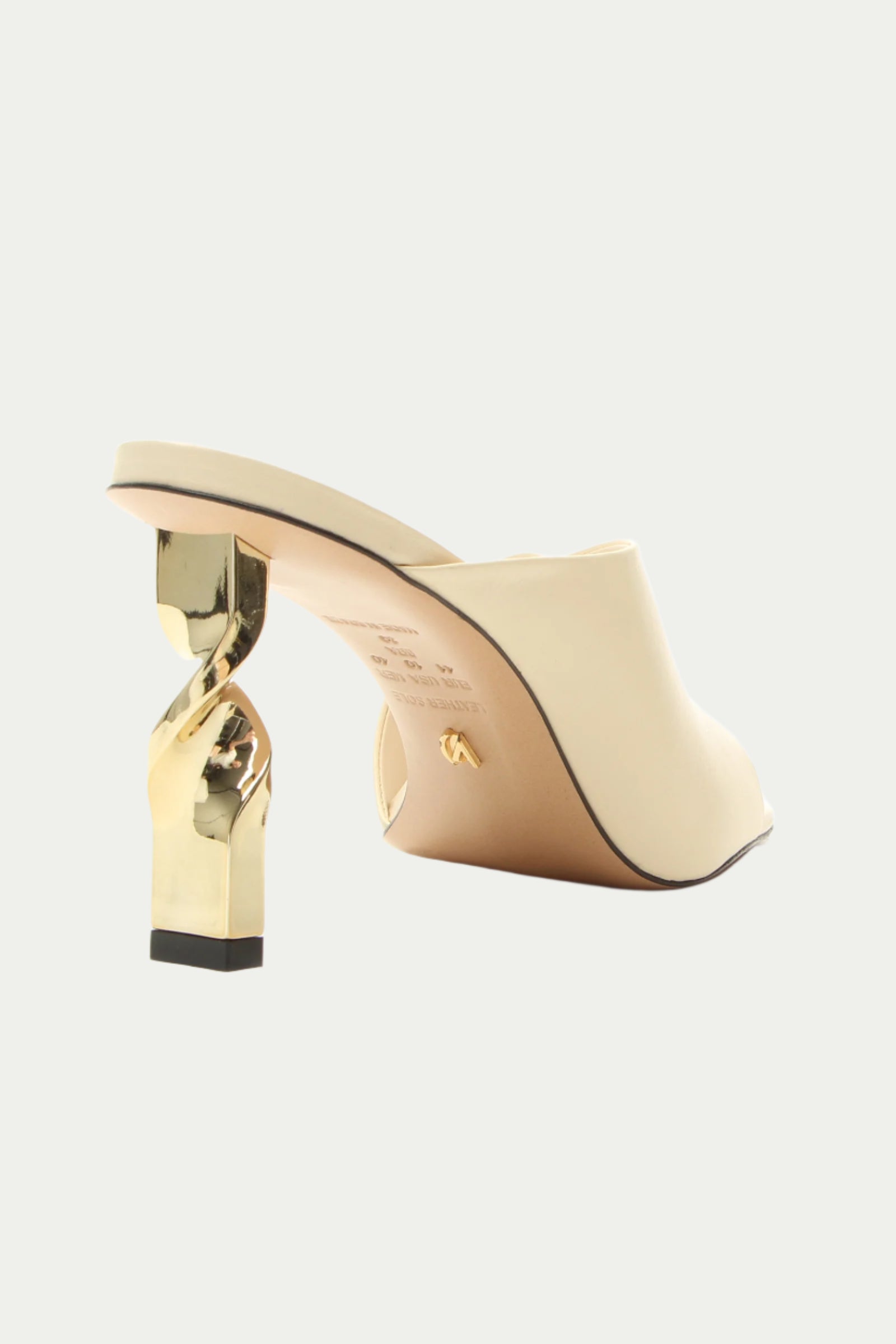 The Bariloche Leather Sculpted Heel Mule in white features a cream tone and a uniquely twisted gold heel, shown against a plain light background.