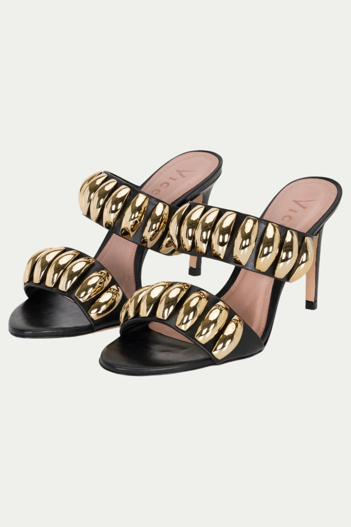 The GOLDEN VOLUME HEEL SANDAL is a black and gold pair of stilettos with two wide straps, each decorated with shiny gold oval embellishments.