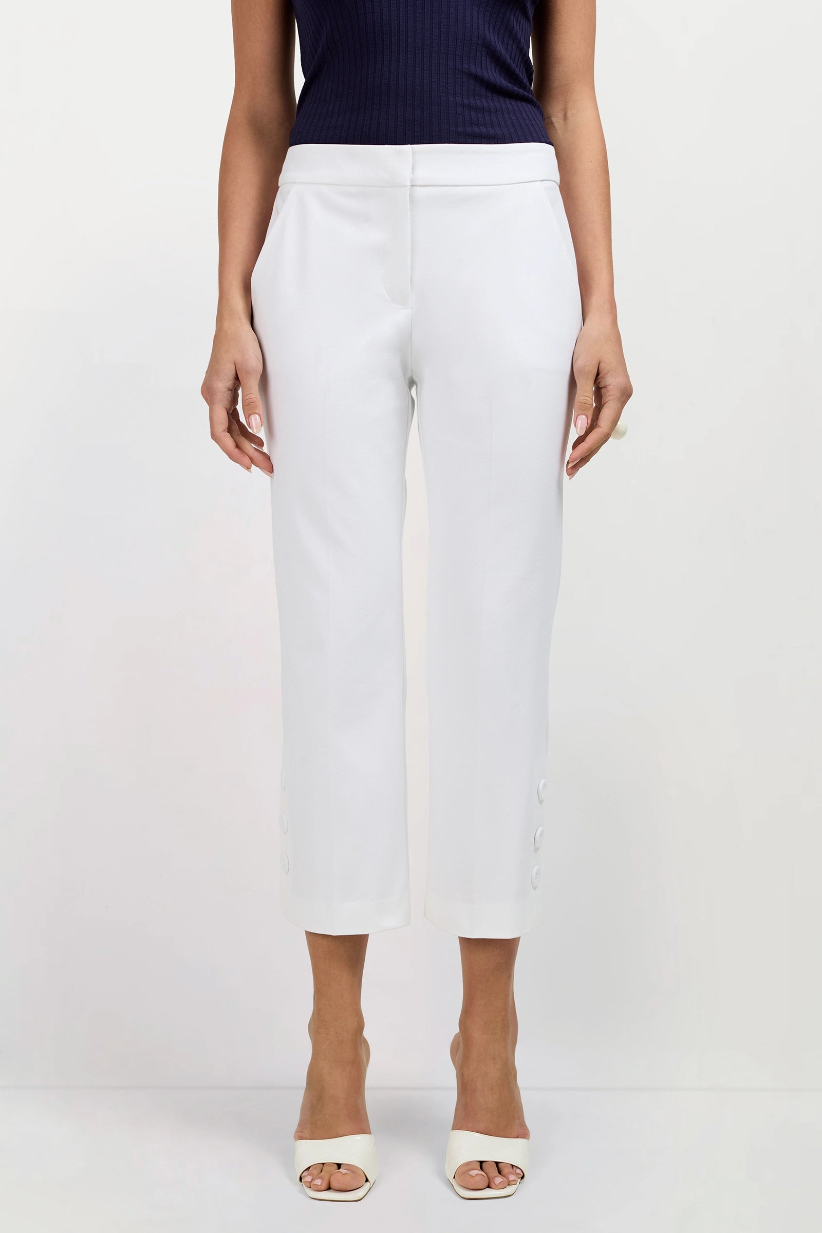 A person in Ore Button-Hem Cropped Pants, styled with a dark sleeveless top and white open-toed heels, stands against a plain light background.