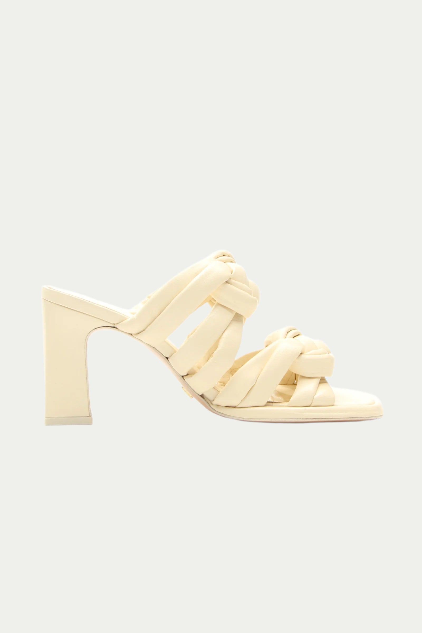 The Montpellier Leather Knot Heel Sandal in white features woven braided straps, an open toe, and a high heel, shown against a light neutral background.