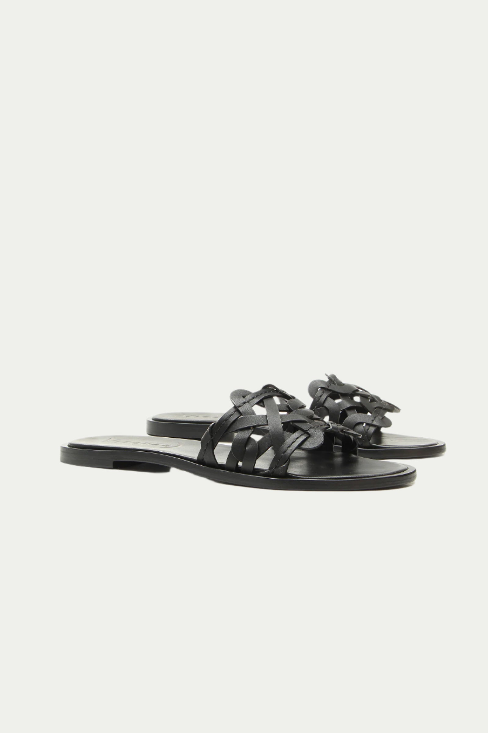 The Haia Black Woven Leather Slide Sandal features black woven leather straps and flat soles, displayed against a plain white background.