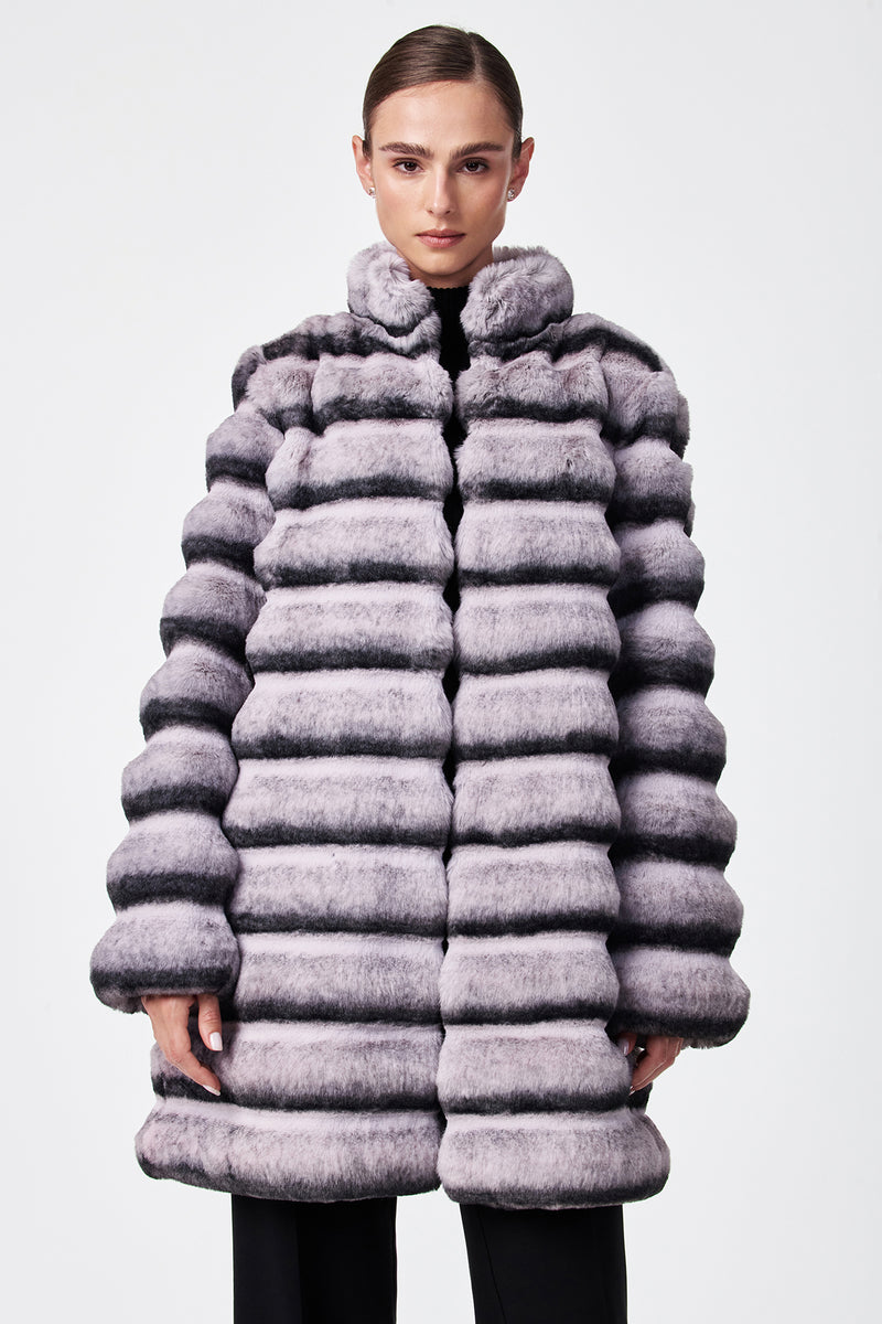 A person models the Mikel 2 Faux Fur Mid-Length Coat, featuring thick, striped light gray and black faux fur with a high collar and puffy horizontal quilted design, standing against a plain white background.