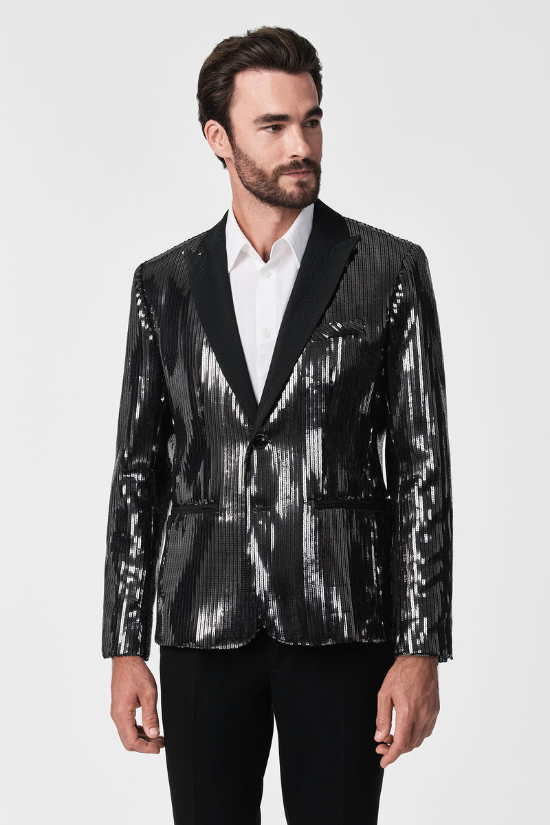 A man with dark hair and a beard models the shiny black Coleman Blazer over a white dress shirt and black pants, standing against a plain white background.