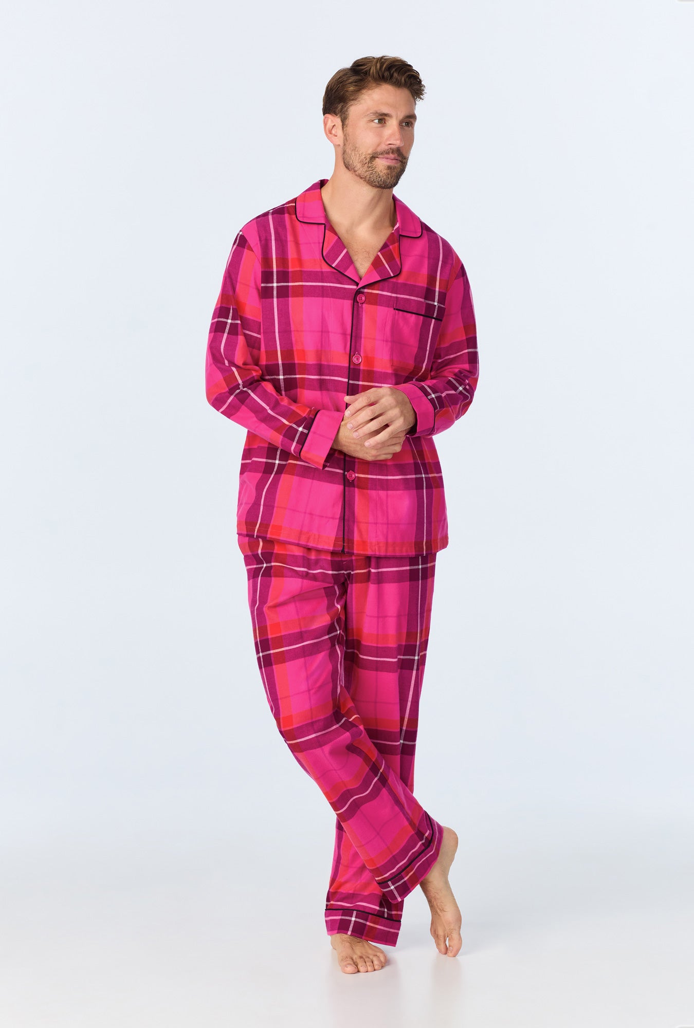 A man poses barefoot in the Aurora Plaid Mens Long Sleeve Long Pant Flannel PJ Set, featuring a bright pink plaid button-up top and matching pants, against a plain light background.