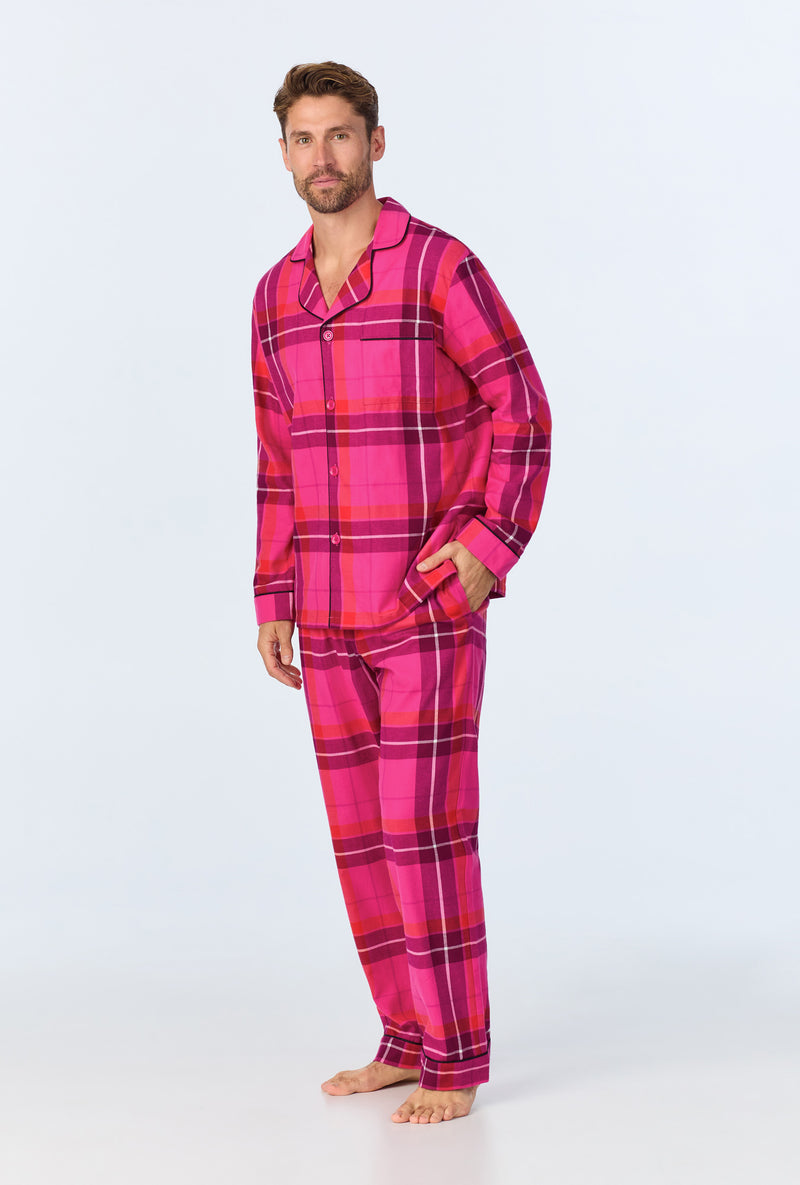 A man stands barefoot in the Aurora Plaid Mens Long Sleeve Long Pant Flannel PJ Set—featuring a bright pink and red plaid button-up shirt and matching pants—posing against a plain light background.