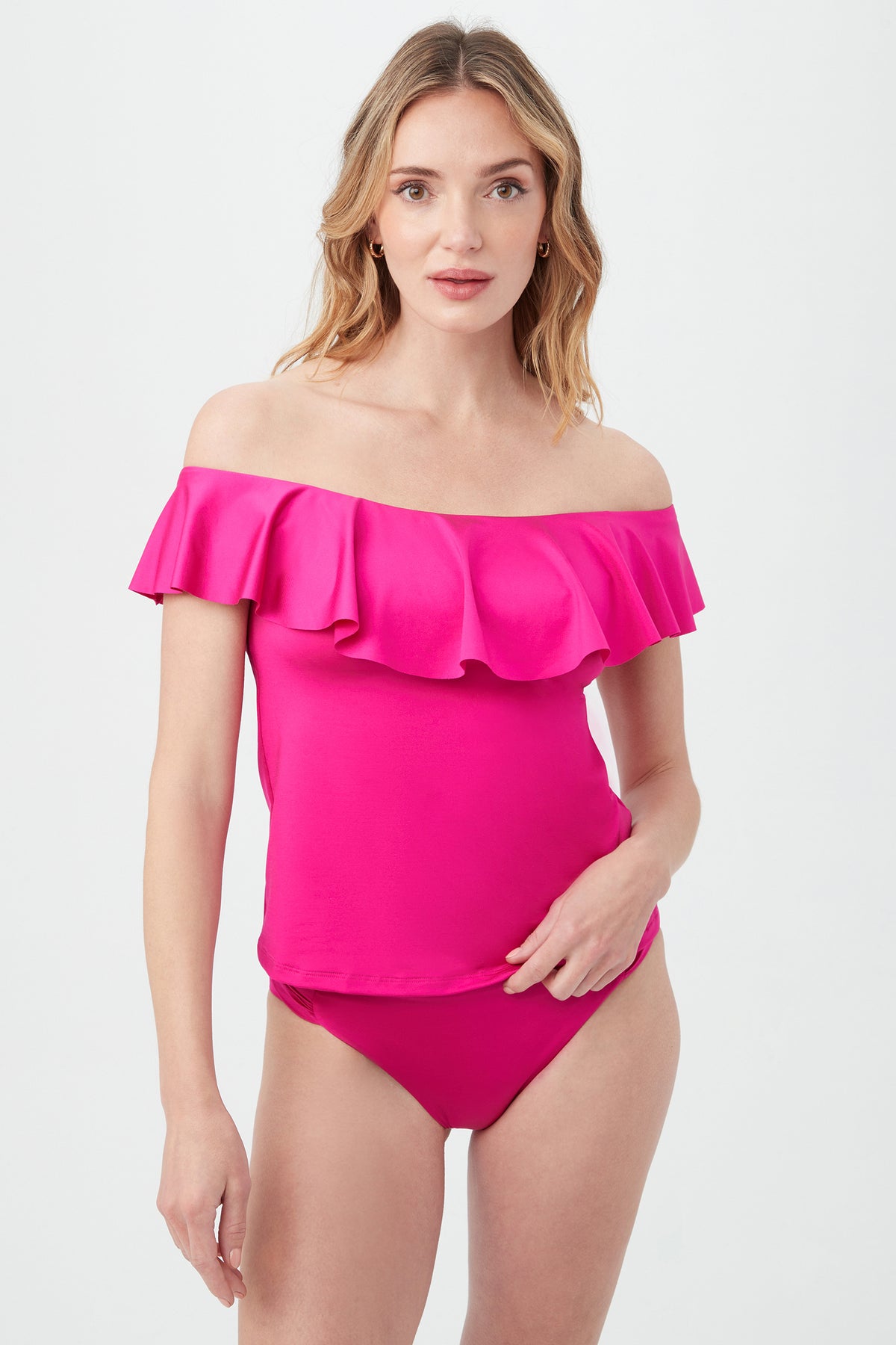 A woman models the Women's Monaco Off The Shoulder Ruffle Tankini Swim Top in Sangria, paired with matching bikini bottoms, standing against a plain light background and looking at the camera with a neutral expression.