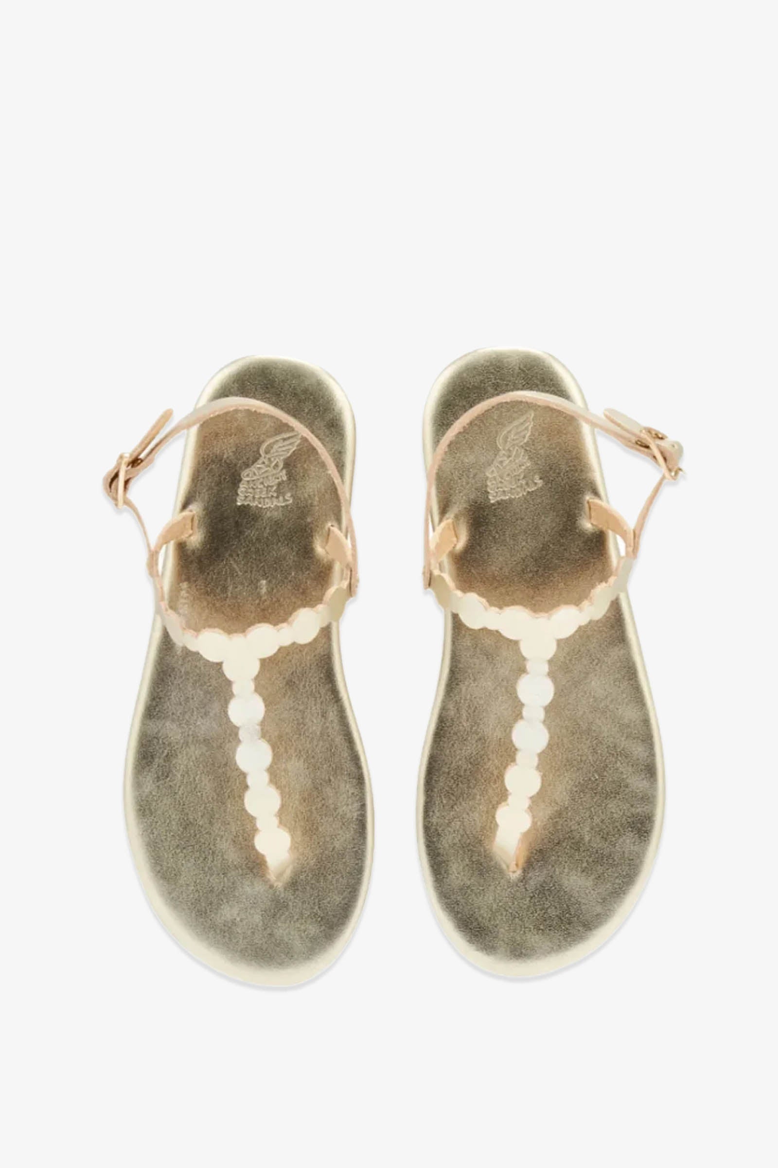 A pair of Ancient Greek Sandals Velos flat, tan leather sandals featuring scalloped straps and circular white embellishments, viewed from above on a white background.