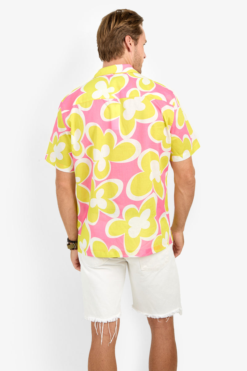 A person stands facing away, wearing the Felix Camp Shirt in pink and yellow floral print with white frayed shorts against a plain white background.