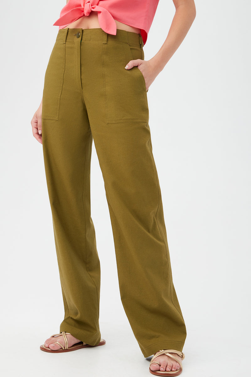 Someone models the Antonia Pant in olive green, featuring a wide-leg cut and front pockets, paired with a coral pink tie-front top and beige sandals. The photo has a plain white background and does not show the model’s head.