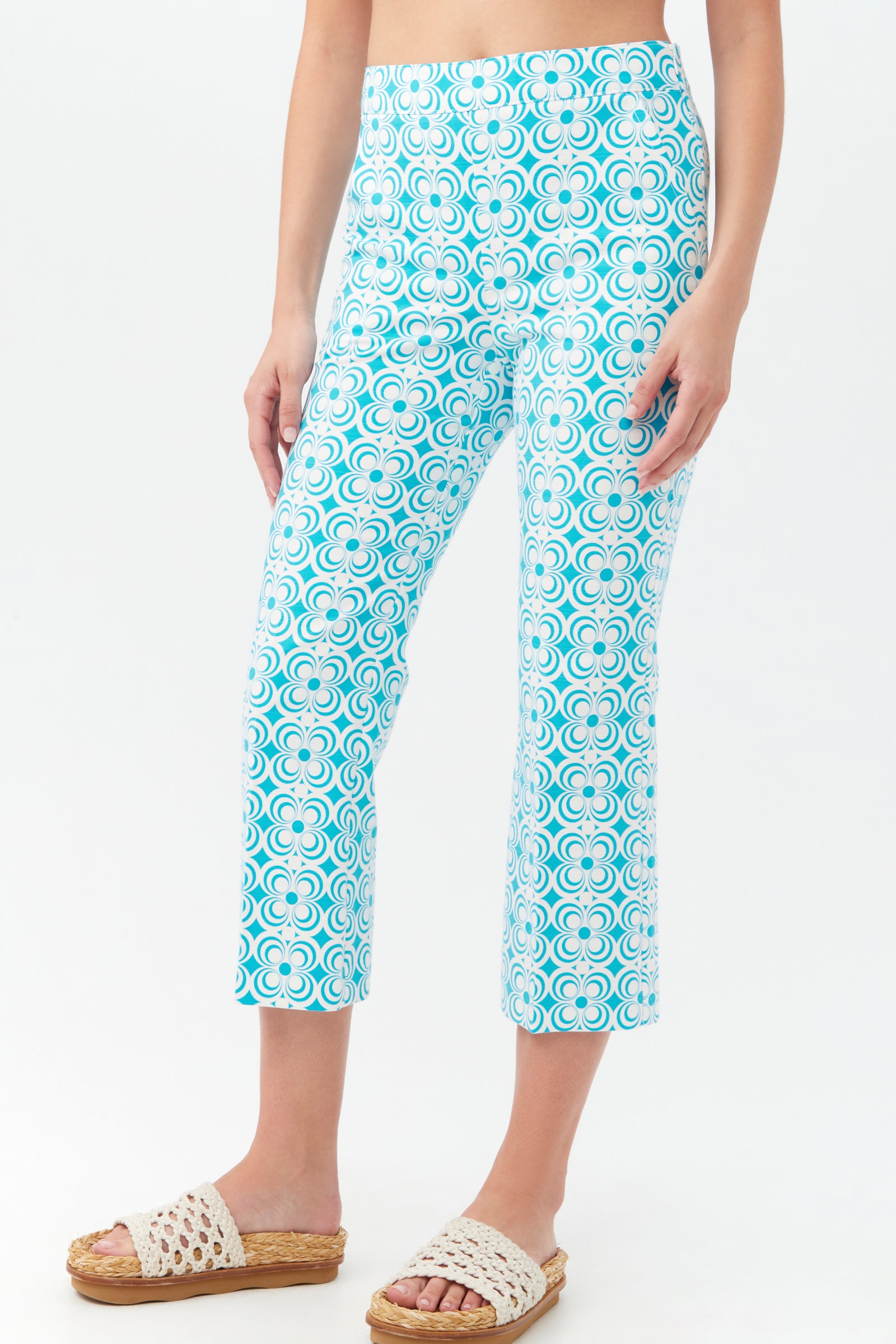A person wearing Flaire 2 Pant—cropped, blue and white geometric patterned pants—paired with woven slide sandals. The background is plain white.
