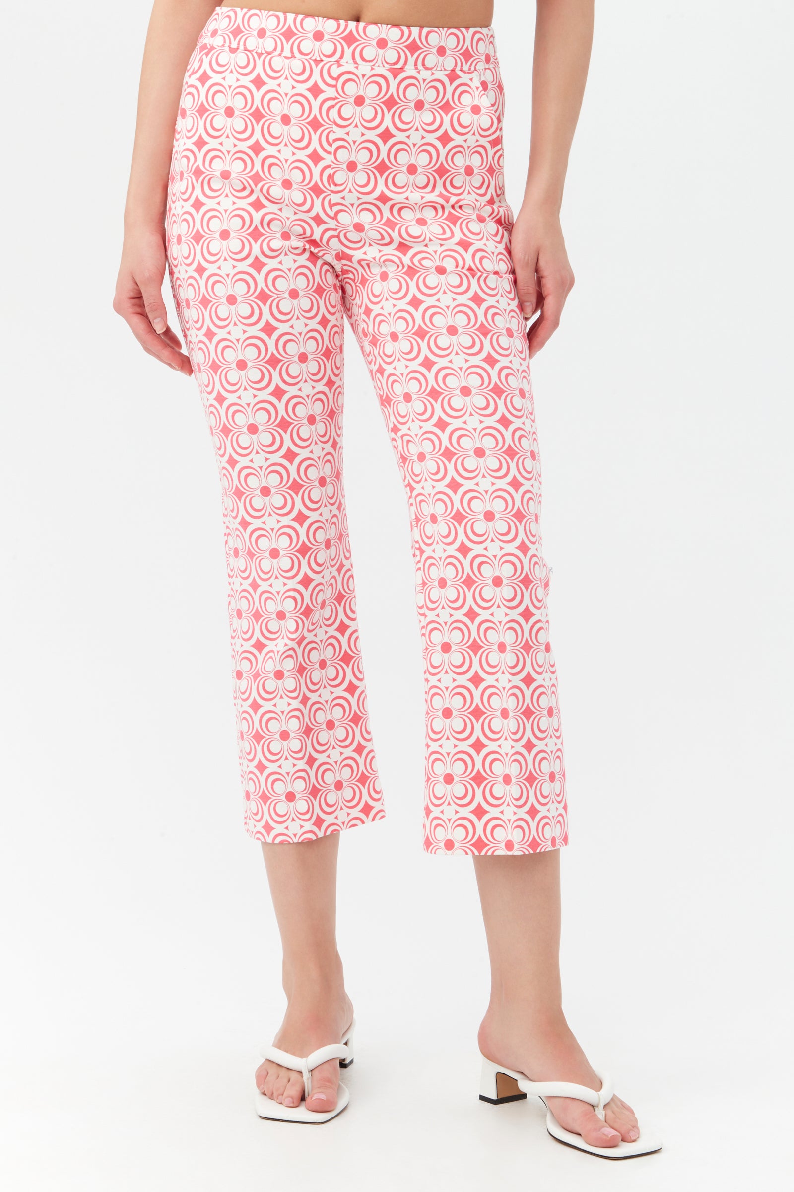 A person wearing the Flaire 2 Pant in Positano Pink, featuring a high waist and cropped fit with a geometric pattern, stands in white sandals against a plain white background.