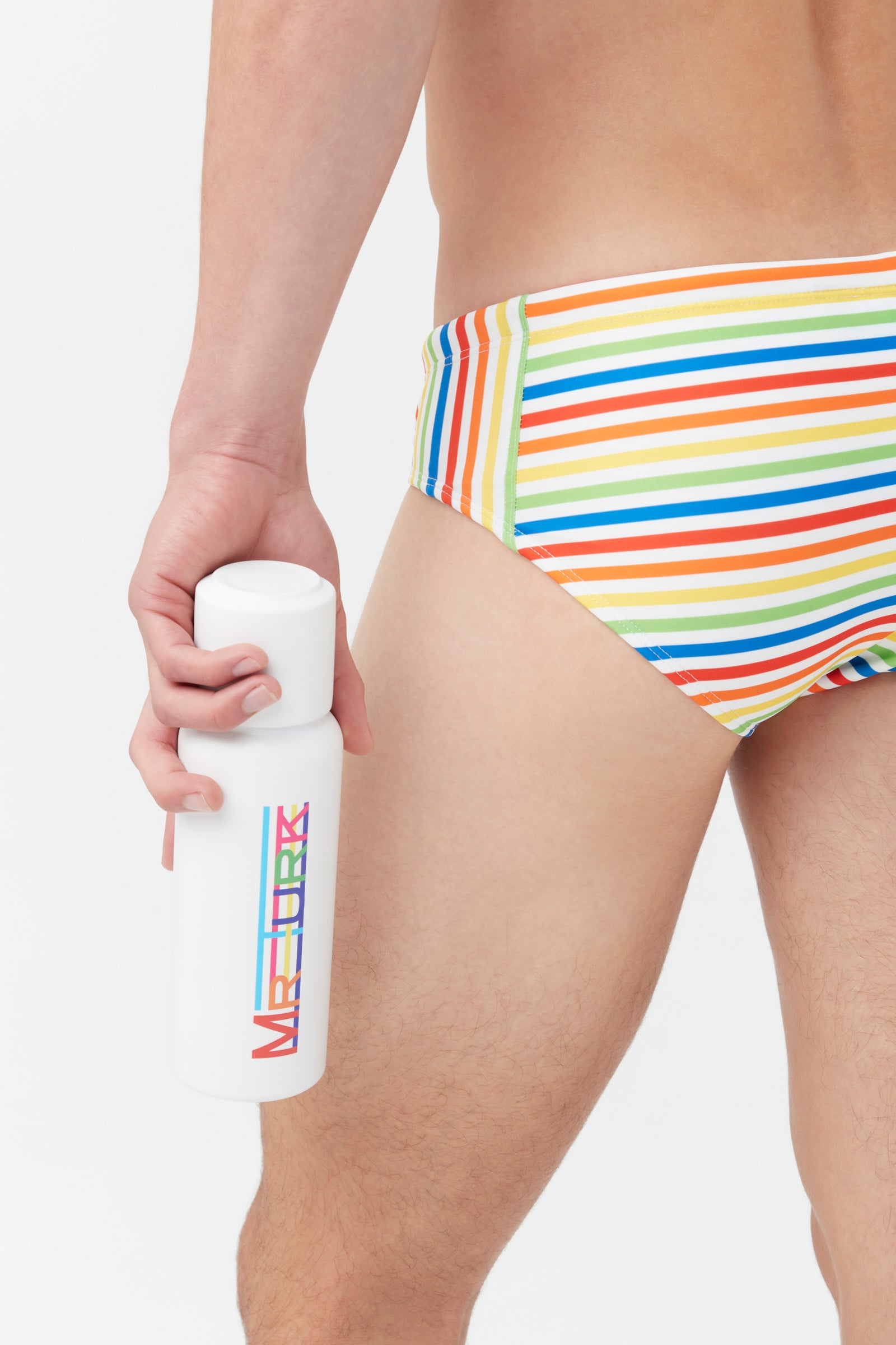 A person holds the Mr Turk Pride Water Bottle, which is white with colorful MR TURK lettering, while wearing rainbow-striped swim briefs against a plain white background.
