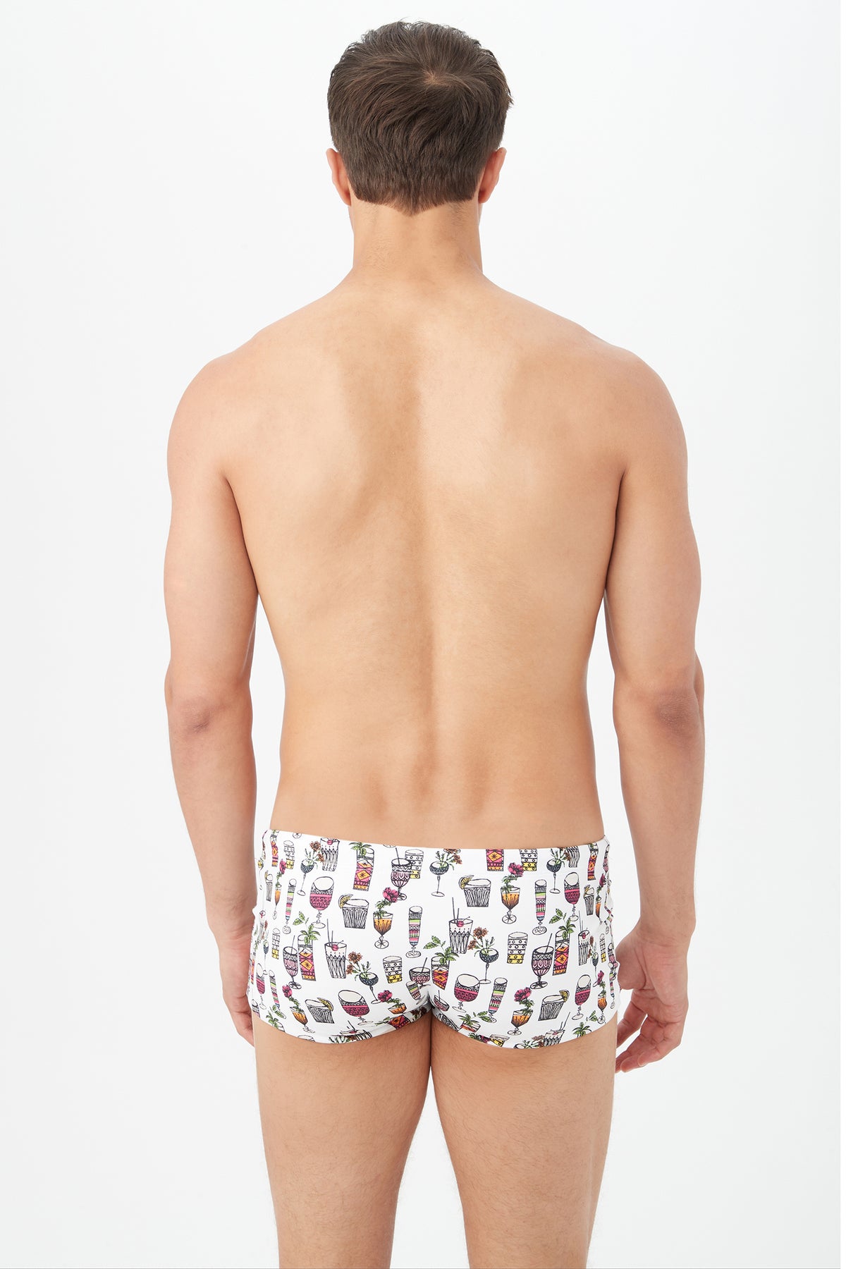 A man faces away from the camera, wearing the Sorrento Swim Trunk - Happy Hour Swim Knit, featuring a white base with colorful cocktail glass prints. The background is plain white.