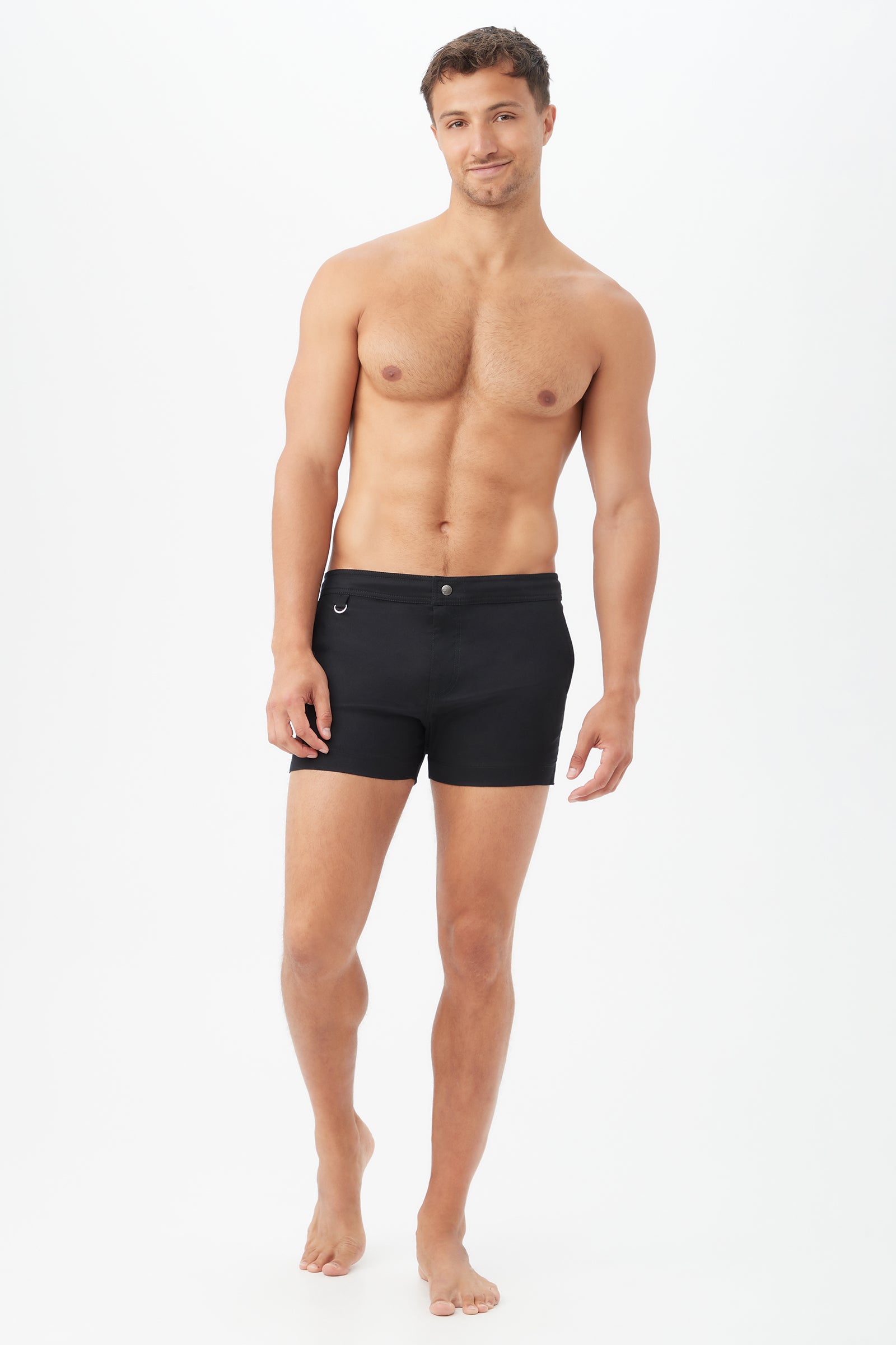 A barefoot man smiles against a white background, wearing fitted Chico Swim Trunk - Metallic Swim Woven in black.