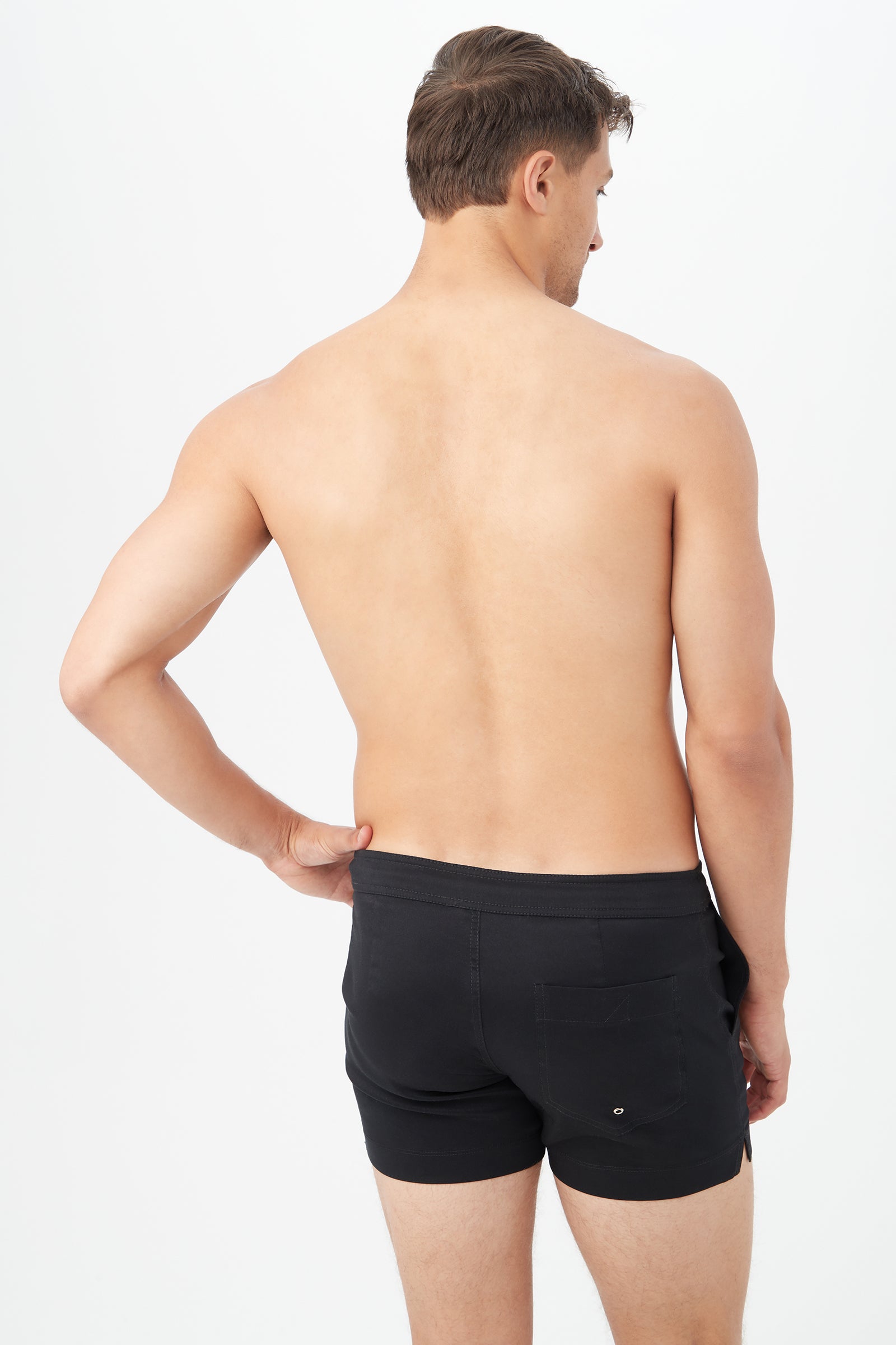 A shirtless man with short brown hair faces away, wearing the Chico Swim Trunk - Metallic Swim Woven in black with a back pocket, set against a plain white background.