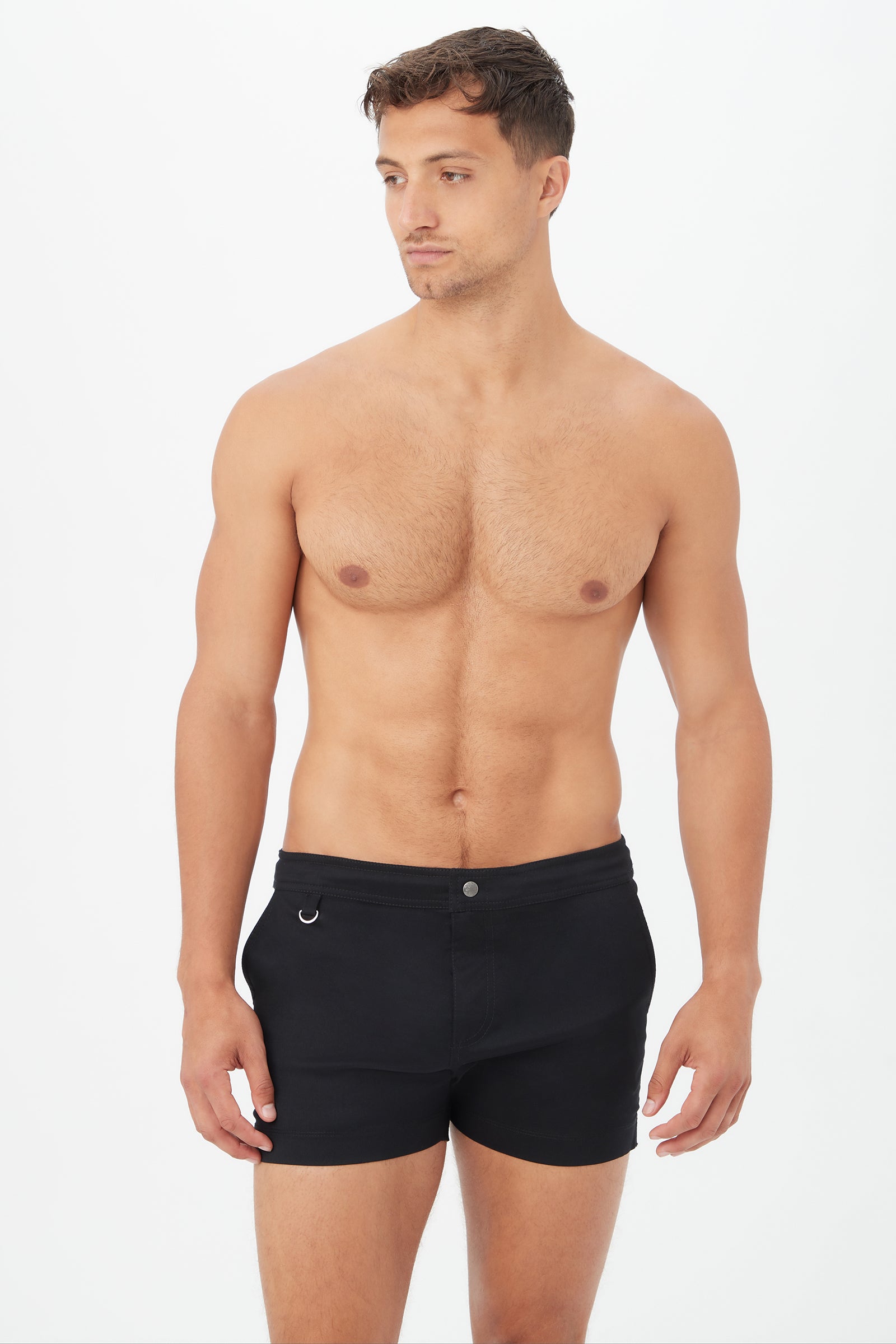 A shirtless man models the Chico Swim Trunk - Metallic Swim Woven in black, standing against a plain white background, looking slightly left with his arms relaxed by his sides.