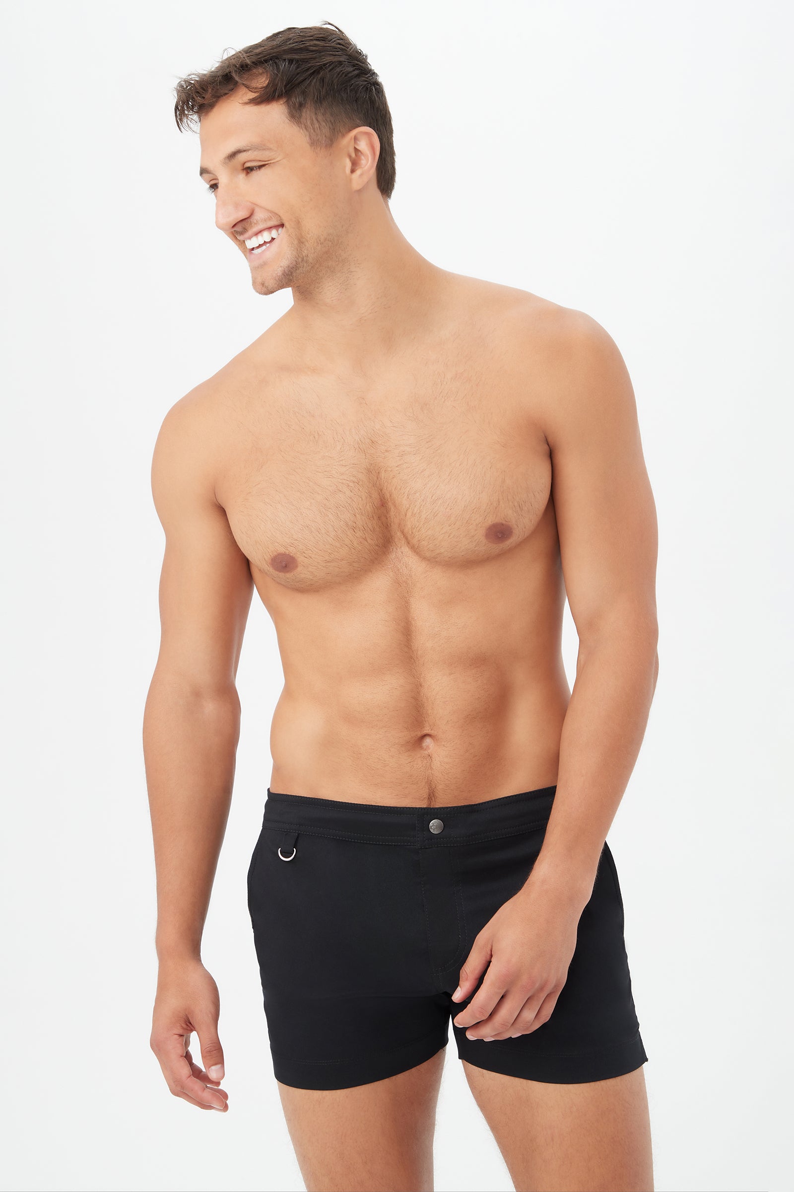 A smiling, shirtless man with short brown hair stands against a plain white background, wearing the Chico Swim Trunk - Metallic Swim Woven in black and looking slightly to the side.