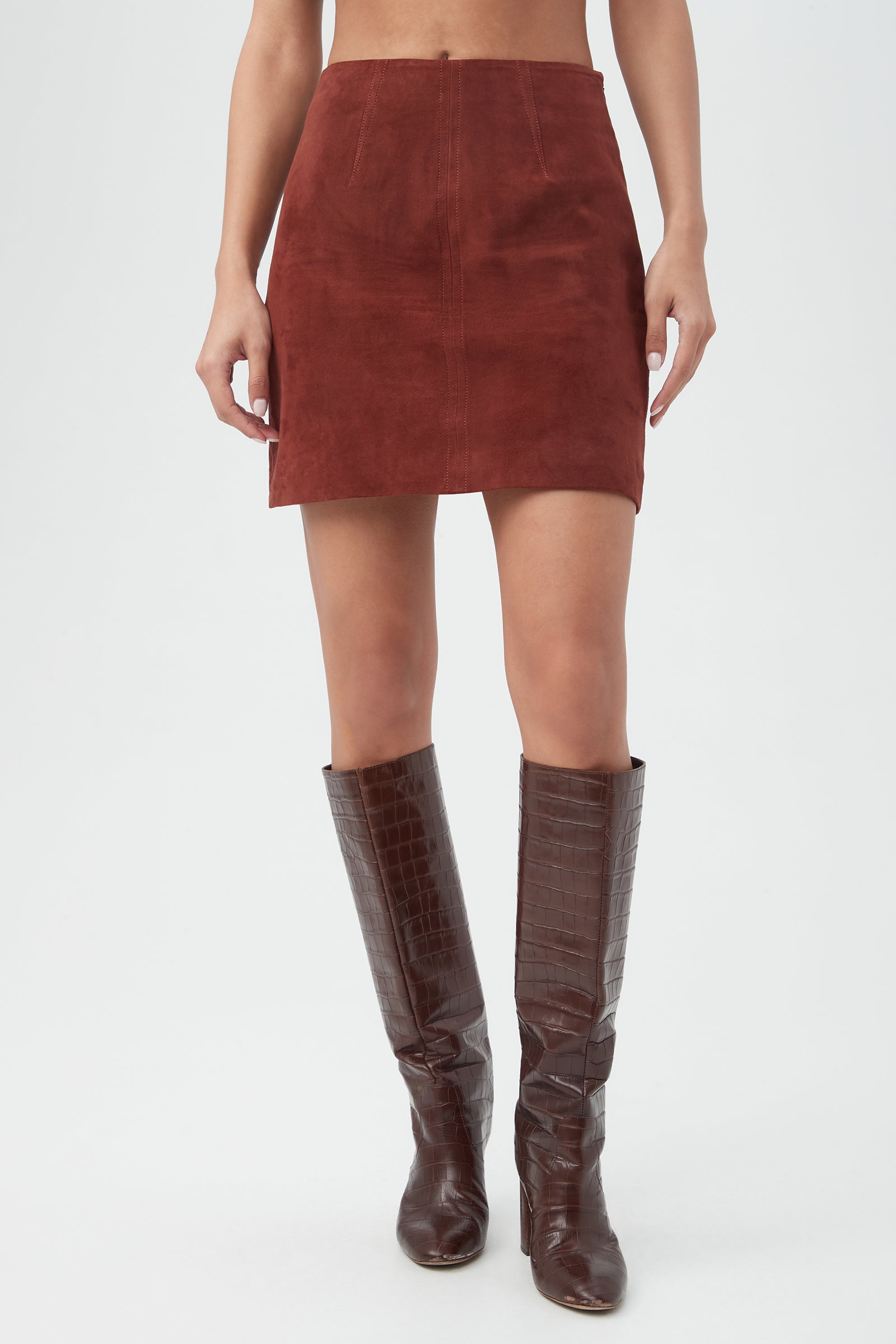 A person wearing the High Waisted Rico 2 Skirt in mahogany and knee-high, dark brown crocodile-textured boots stands against a plain white background.