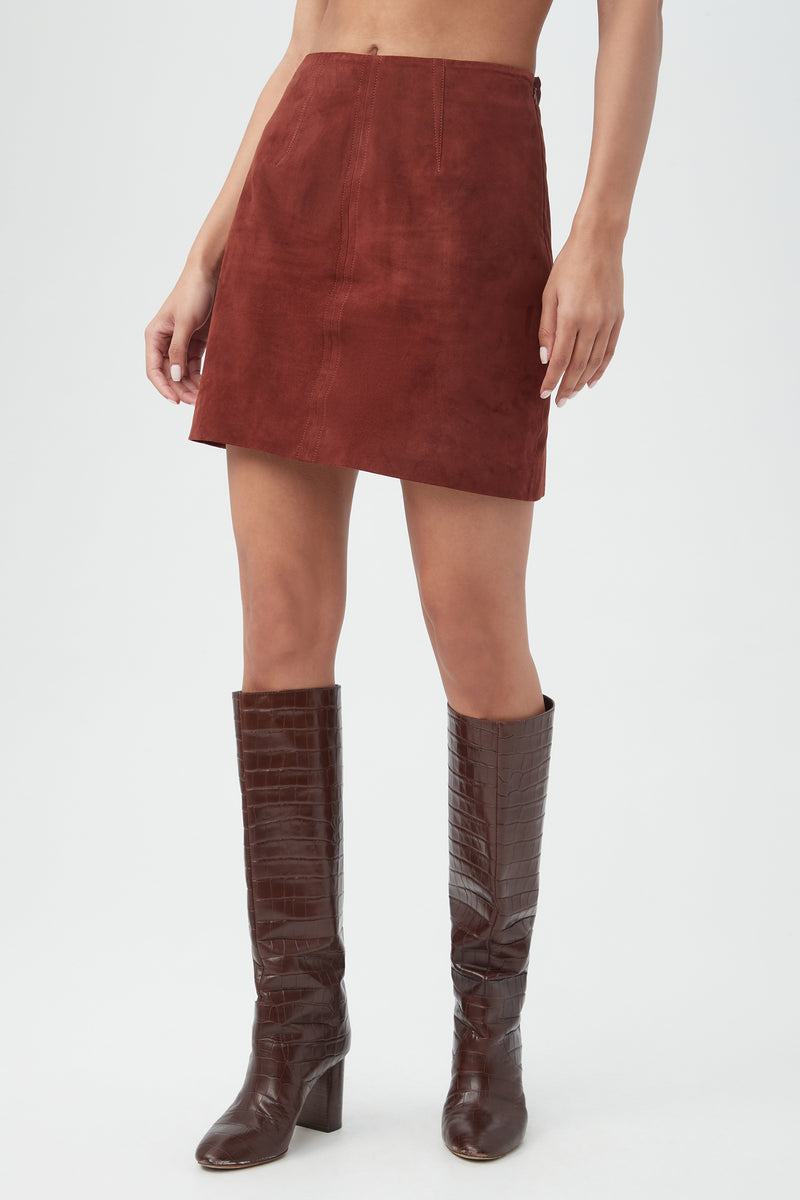 A person wearing the High Waisted Rico 2 Skirt in reddish-brown suede and dark brown, knee-high, crocodile-textured boots stands against a plain light background.