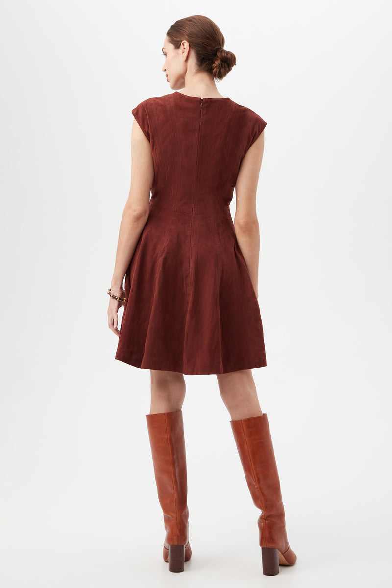 A woman with brown hair in a bun wears the Sabi Dress, a short-sleeve, knee-length dark red dress, paired with tall brown boots. She stands facing away to display the back of her outfit against a plain white background.