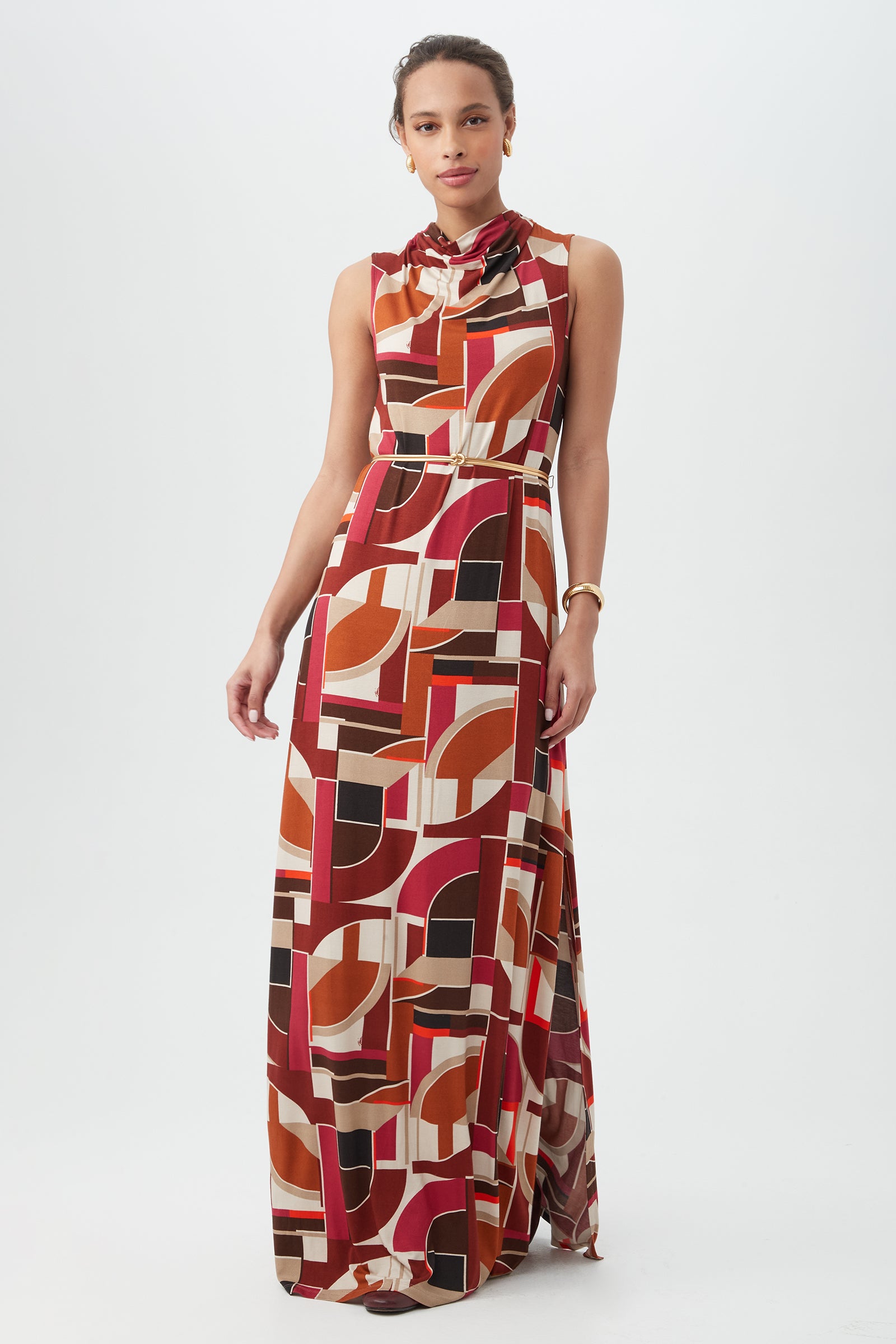 A woman wears the Kia Dress in Multi—a long, sleeveless dress with a bold geometric print and a high gathered neckline—standing against a plain white background.