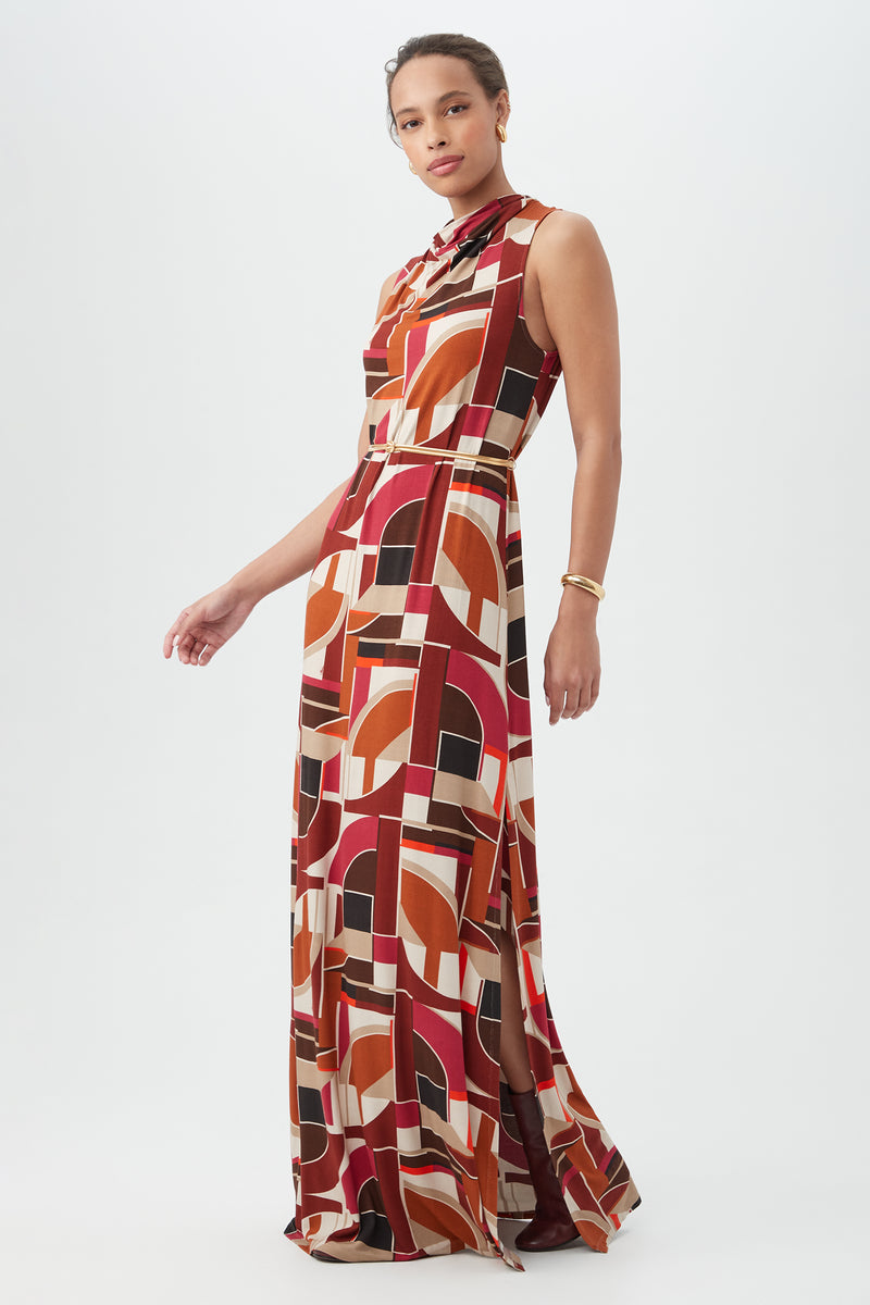 A woman with her hair pulled back and a bracelet stands against a white background, wearing the Kia Dressâ€â€a sleeveless, floor-length dress featuring a bold geometric pattern in red, orange, black, and beige.