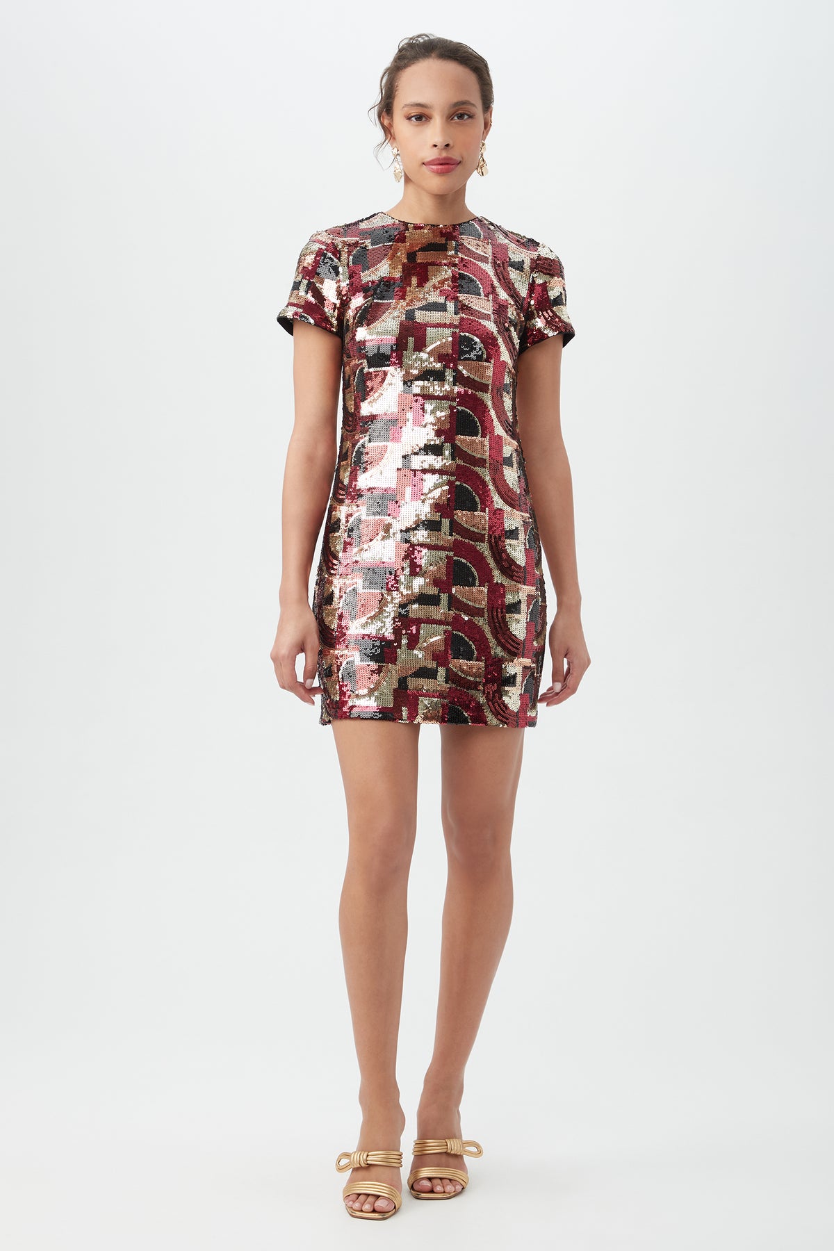A woman stands facing forward against a white background, wearing the Lupine 2 Galerie Arte Sequin Short-Sleeve Shift Dress in multi, styled with hoop earrings, red lipstick, and gold strappy heels.