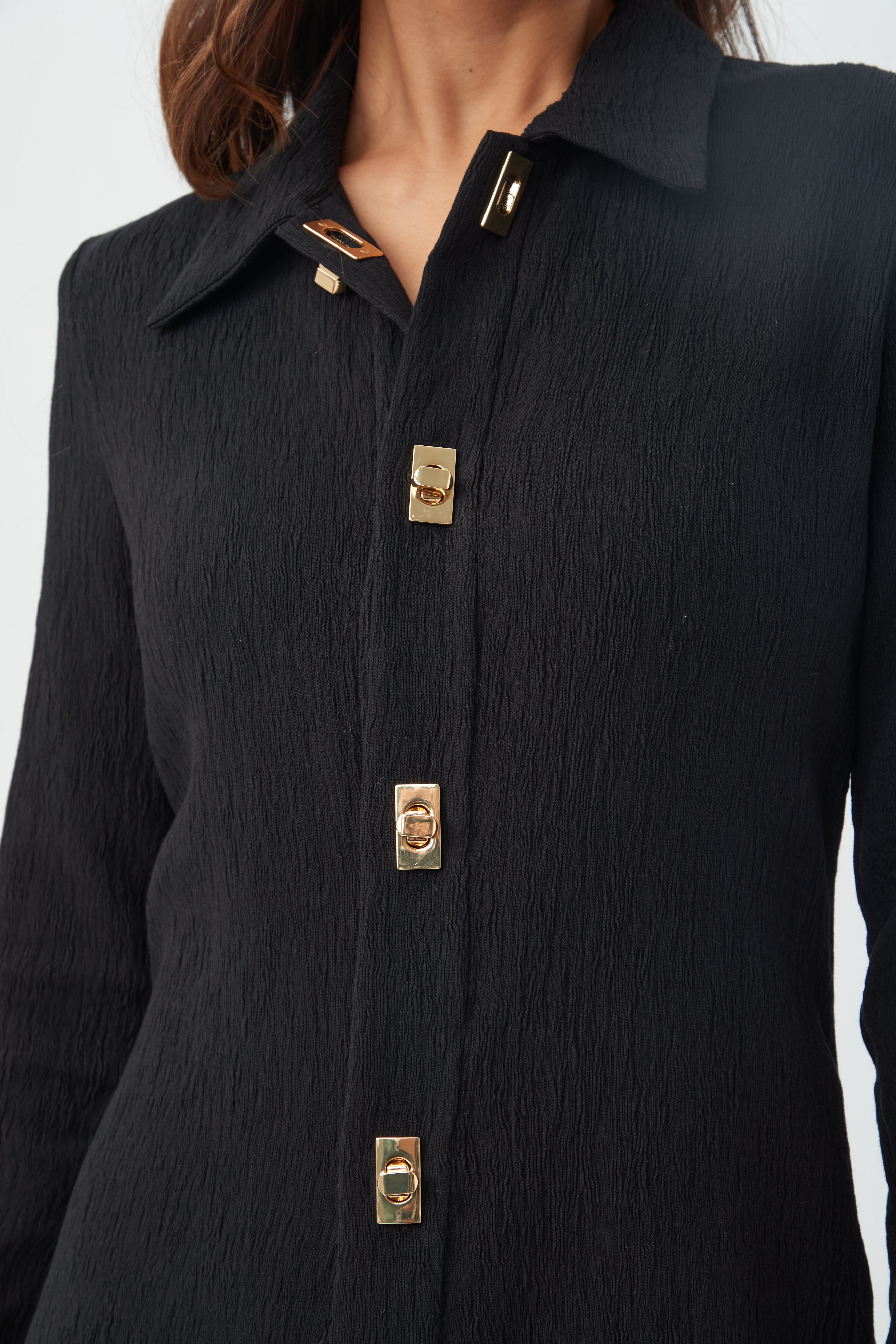 A woman wears the Barika Dress, a textured black collared shirt dress with gold rectangular buttons, shown from shoulders to hips against a plain background.