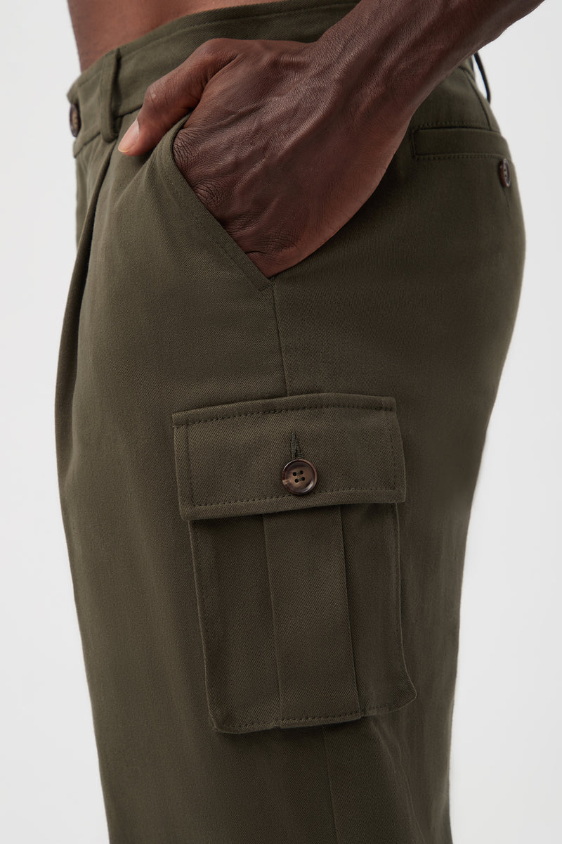 A close-up side view of a person wearing the Lincoln Heights Cargo Trouser - Brushed Twill in olive green, featuring a buttoned flap pocket and their hand in the side pocket against a plain white background.
