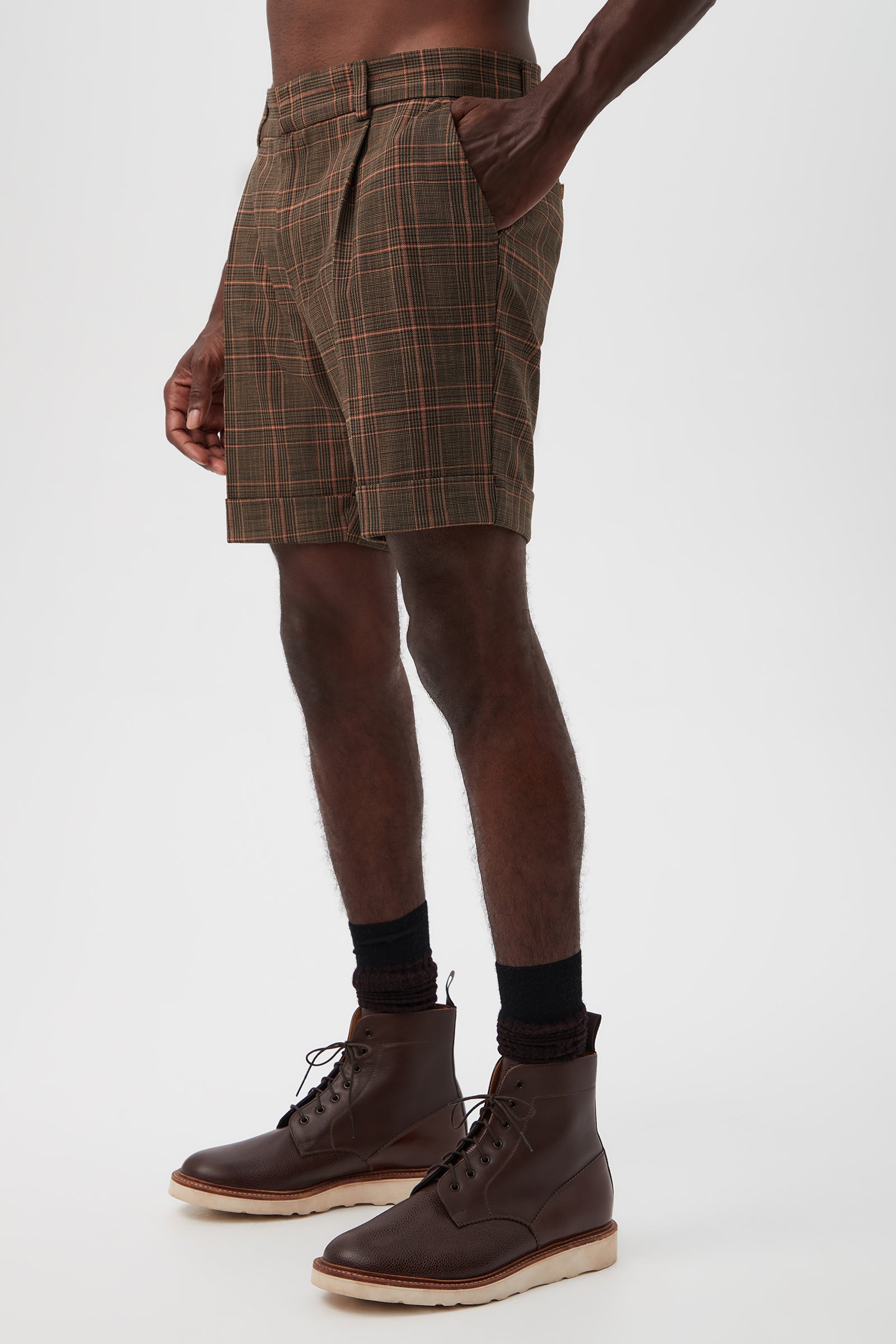 A person wears the Oliver 2 Short - Chaka Check Plaid, paired with dark socks and dark brown lace-up boots. The image, cropped from waist down, highlights the shorts along with the lower torso, legs, and feet against a plain background.