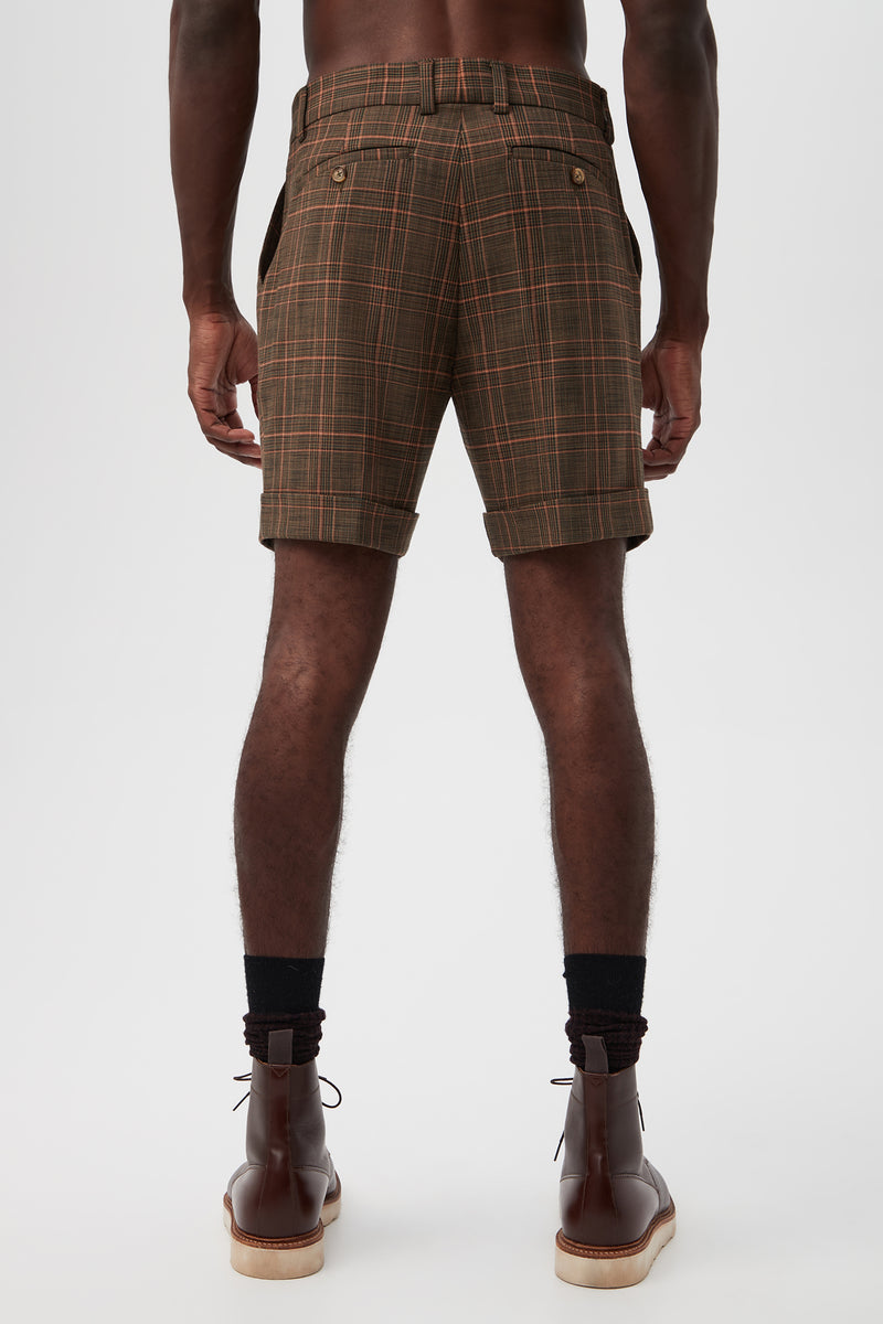 A person stands facing away from the camera against a plain white background, wearing the Oliver 2 Short - Chaka Check Plaid with black socks and brown leather boots.