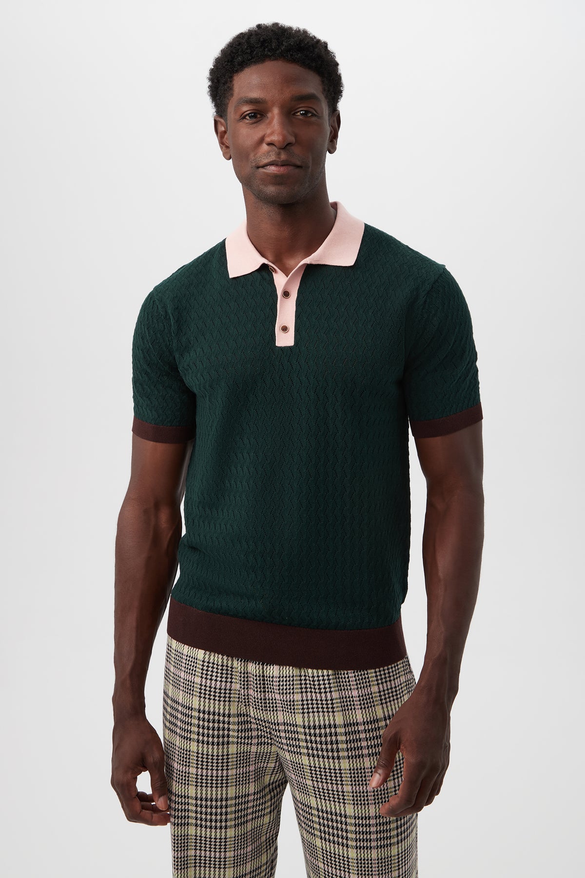 A man faces forward against a plain white background, wearing the Vinny Short-Sleeve Polo in Victoria Lake Multi and cream and brown plaid trousers.