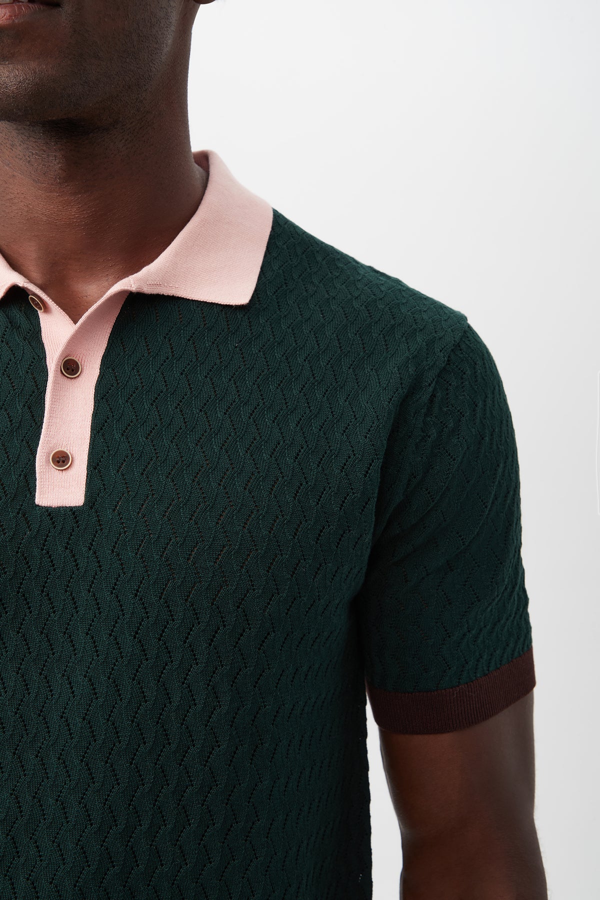 A person wearing the Vinny Short-Sleeve Polo in textured dark green with a pink collar and brown sleeve cuffs, shown from shoulders to mid-chest against a plain background.
