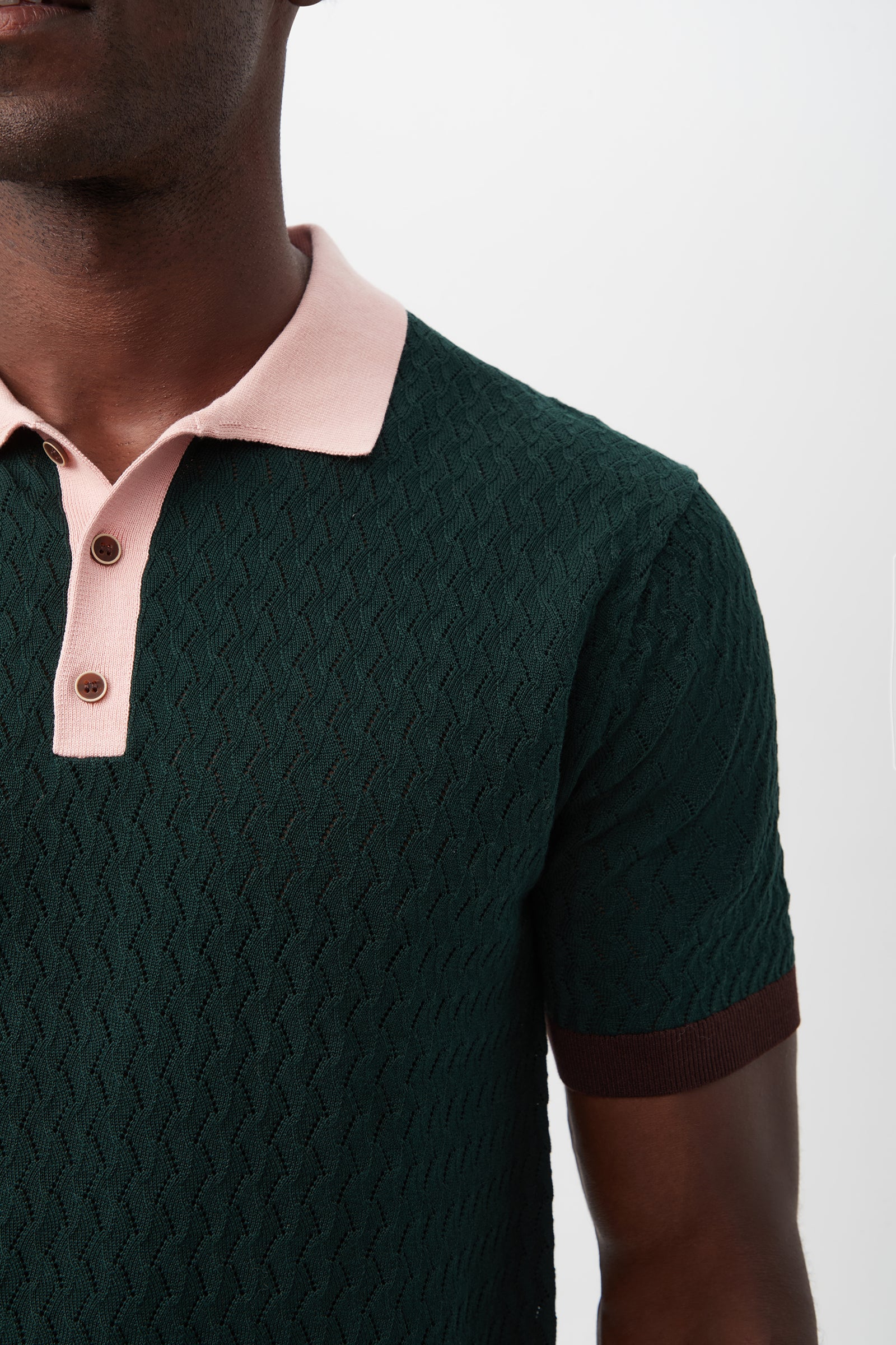 A person wearing the Vinny Short-Sleeve Polo in textured dark green with a pink collar and brown sleeve cuffs, shown from shoulders to mid-chest against a plain background.